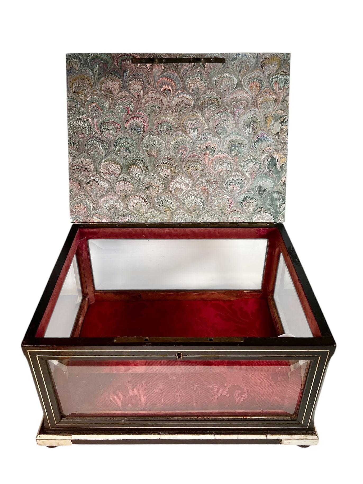 Una exquisita vitrina francesa de mediados del siglo XIX, ricamente chapada en hueso y acabada con cristal biselado en los cuatro lados para ofrecer la máxima luz y visibilidad. El interior está forrado de suntuosa seda adamascada roja, que ofrece