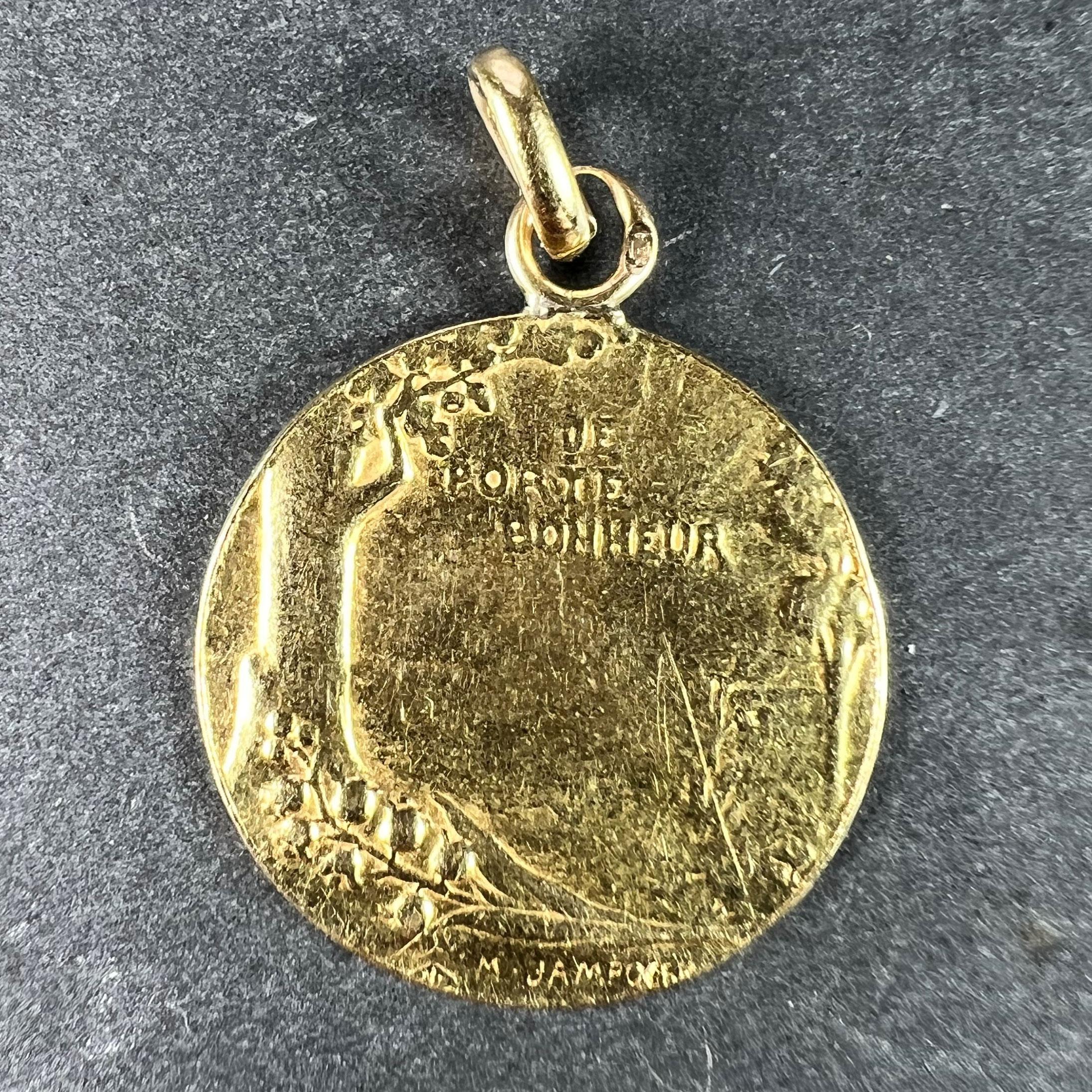 A French 18 karat (18K) yellow gold lucky charm pendant designed as a medal depicting a sunrise over a pastoral scene with lilies of the valley under an oak tree bearing a pair of acorns, with the phrase 'Je Porte Bonheur' (meaning 'I bring good