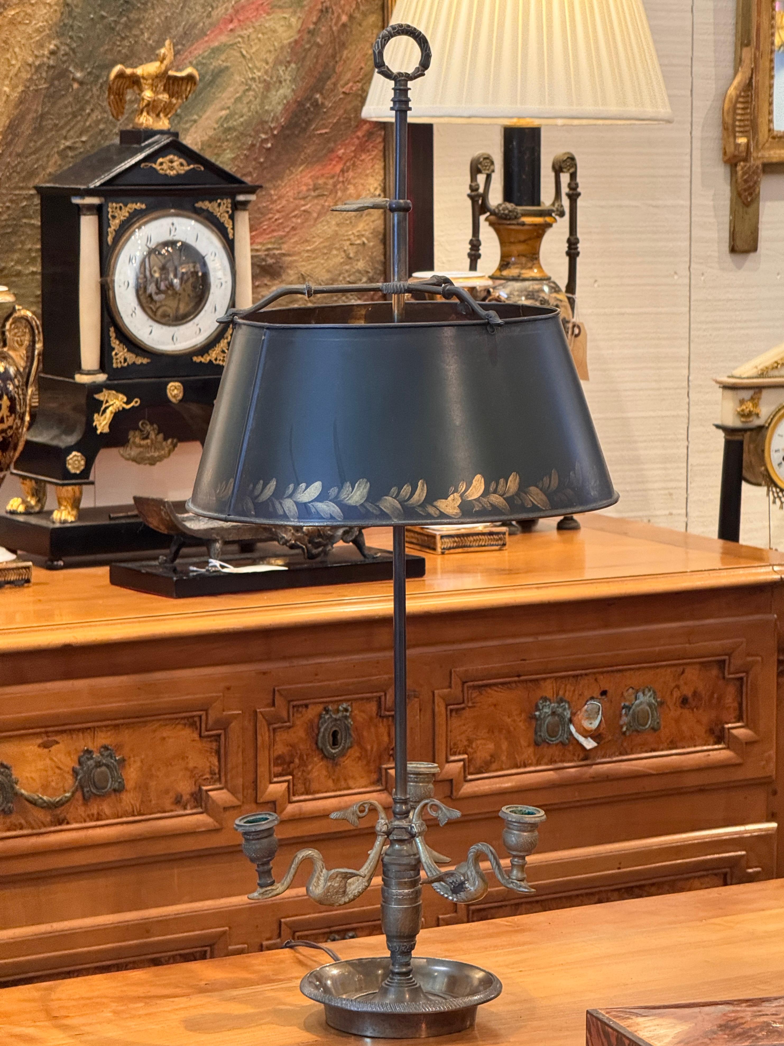 Französische Bouillotte-Lampe mit dunkelgrünem Tole-Schirm mit vergoldetem Blattdekor und verstellbarer Höhe. Der Sockel aus patiniertem Metall trägt drei Arme in Form eines Schwans mit klassischem Motiv. Die Nahaufnahme hebt den detaillierten Guss