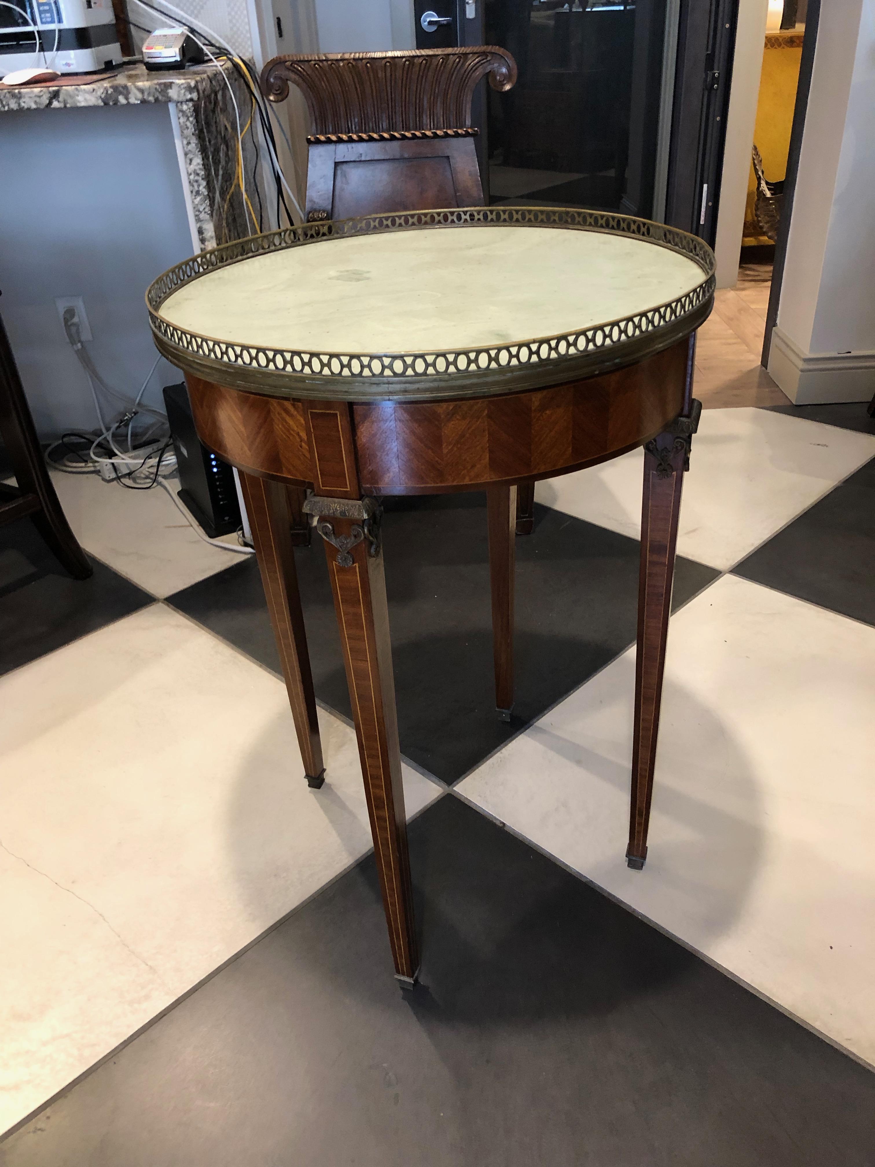 This French Bouillotte table can be used as a side table. It has light mahogany marquetry surrounding the top portion, string design to the legs and a light turquoise marble top. The bronze or brass trim is around the top, bow designs at top of legs