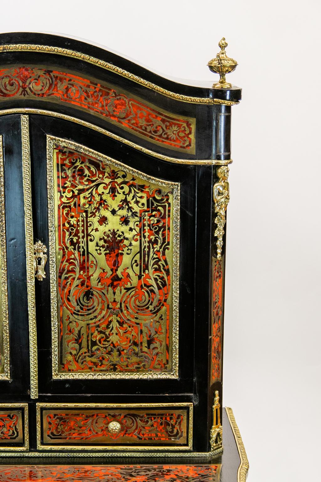 This French Boulle escritoire has profuse brass inlays with arabesques and brass ornamental mounts throughout. The wooden background is ebonized. The drawer pulls out to reveal a sliding gold tooled leather writing surface with storage beneath. The