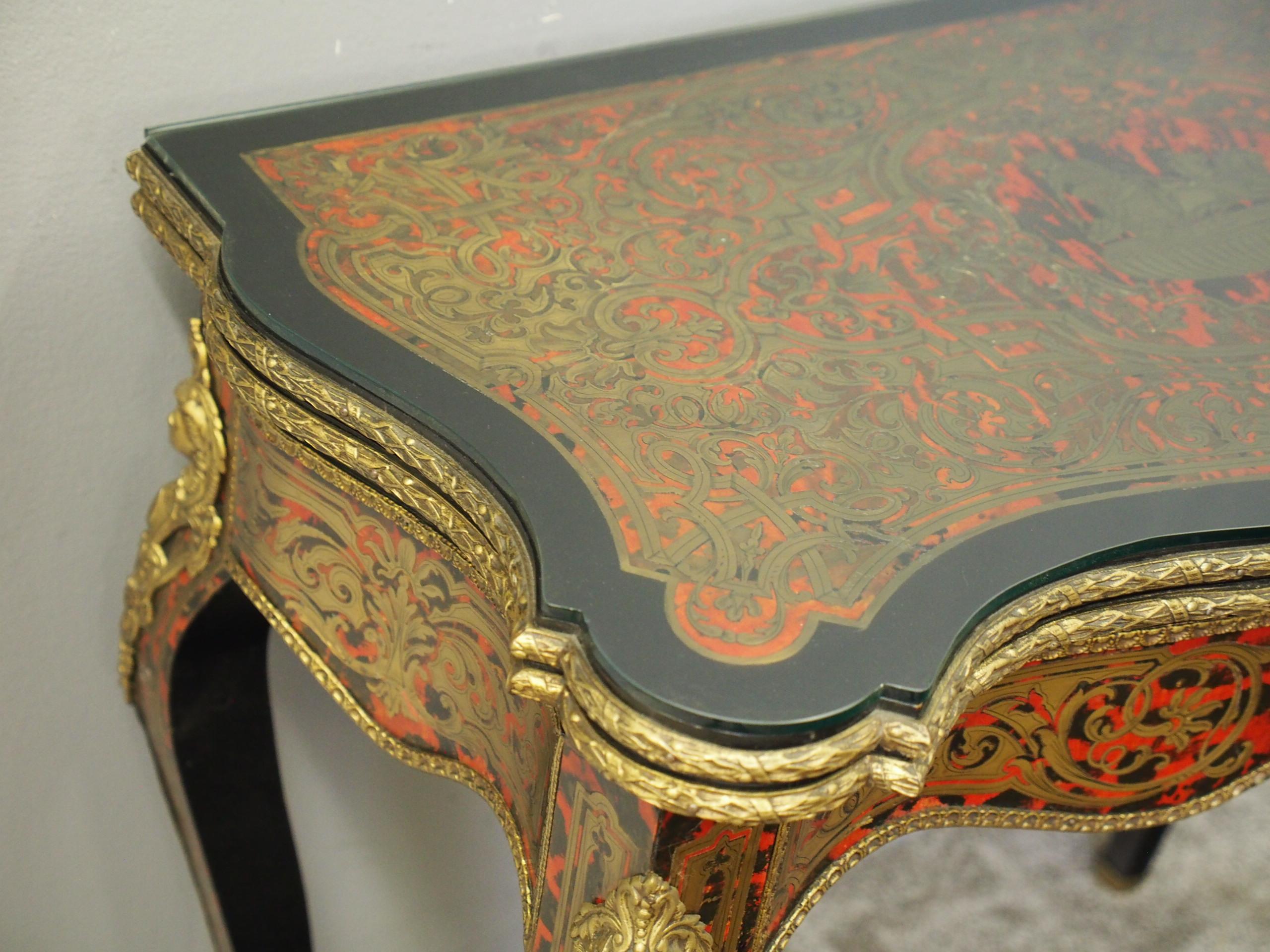 French Serpentine fronted boulle fold-over games table, circa 1870. Covered in red tortoiseshell and engraved brass inlay with foliate and geometric designs centred by a charioteer. It has a hinged top opening to a baize-lined interior. Beneath this