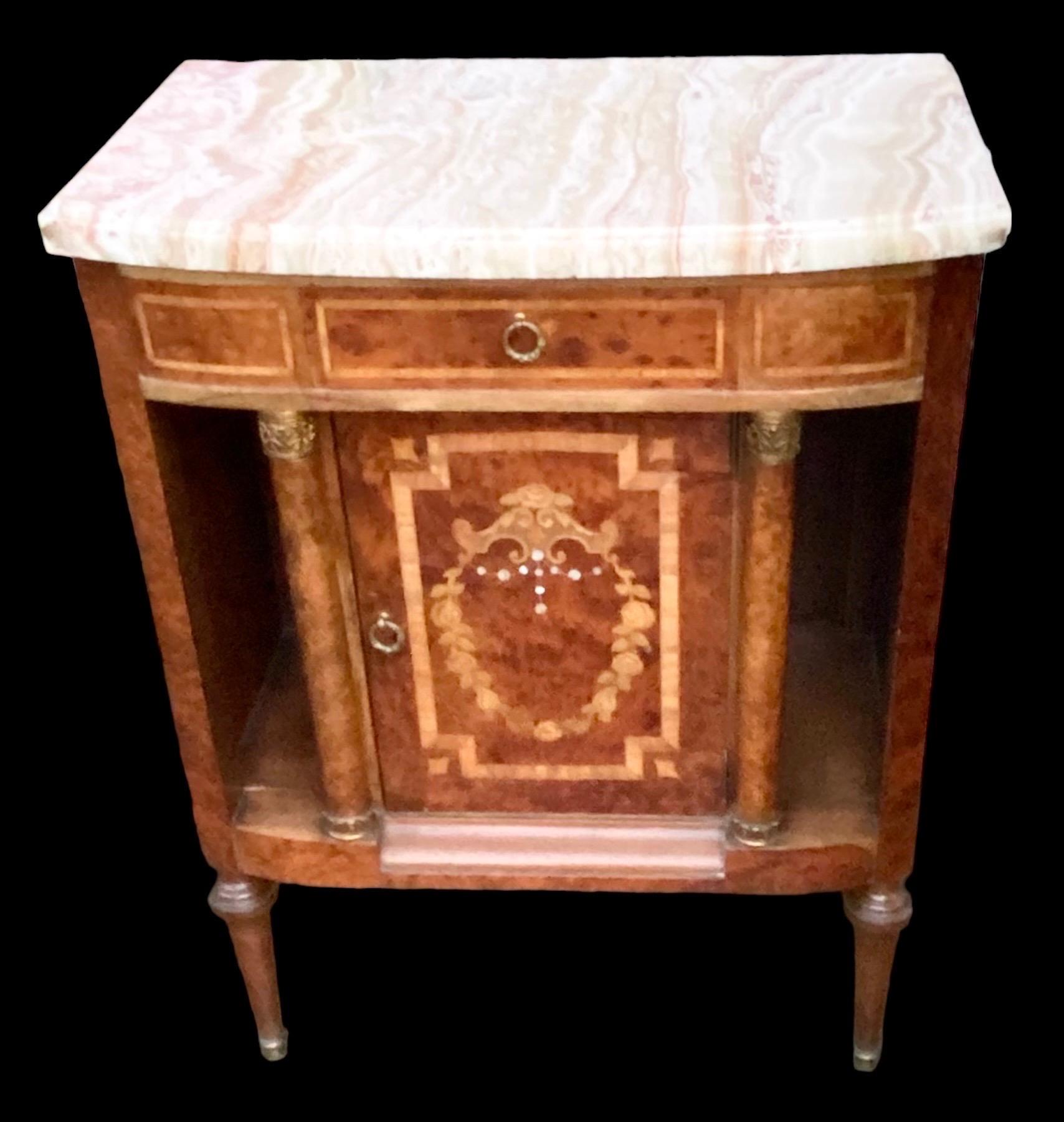 A diminutive, vintage French burled mahogany, satin wood, boxwood and inlaid mother of pearl cabinet with a slightly curved front, topped with a beautifully veined and thick creme marble. 

Underneath is one small inlaid drawer with a bronze ring