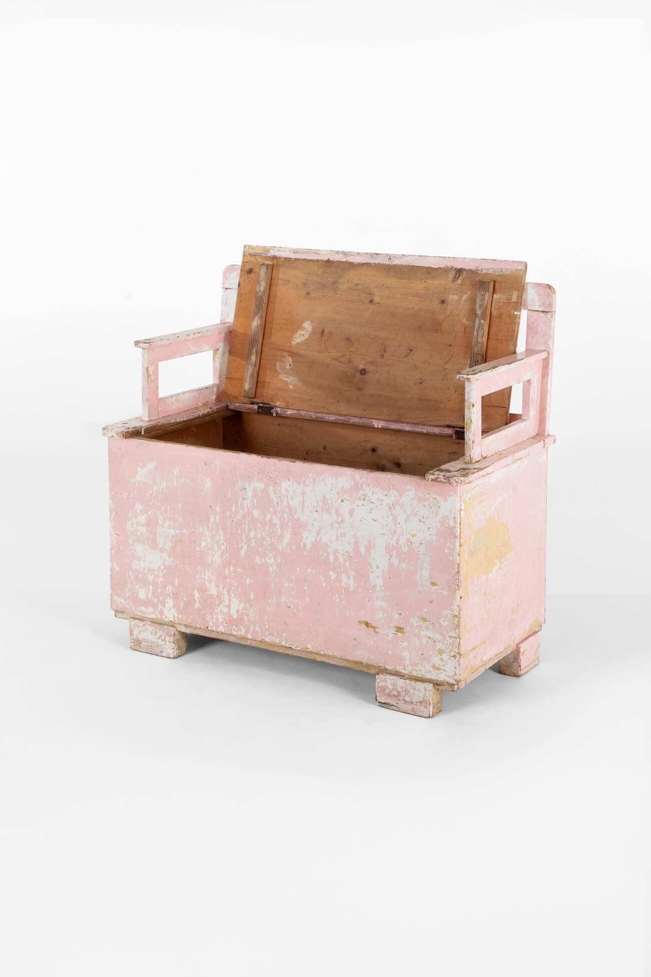 A charming box bench of diminutive proportions in pine with remnants of white and pink paint on the seat and sides.

The ample-sized box has a slatted backrest and two low arms and is raised on four block sturdy block feet.

The bench is very