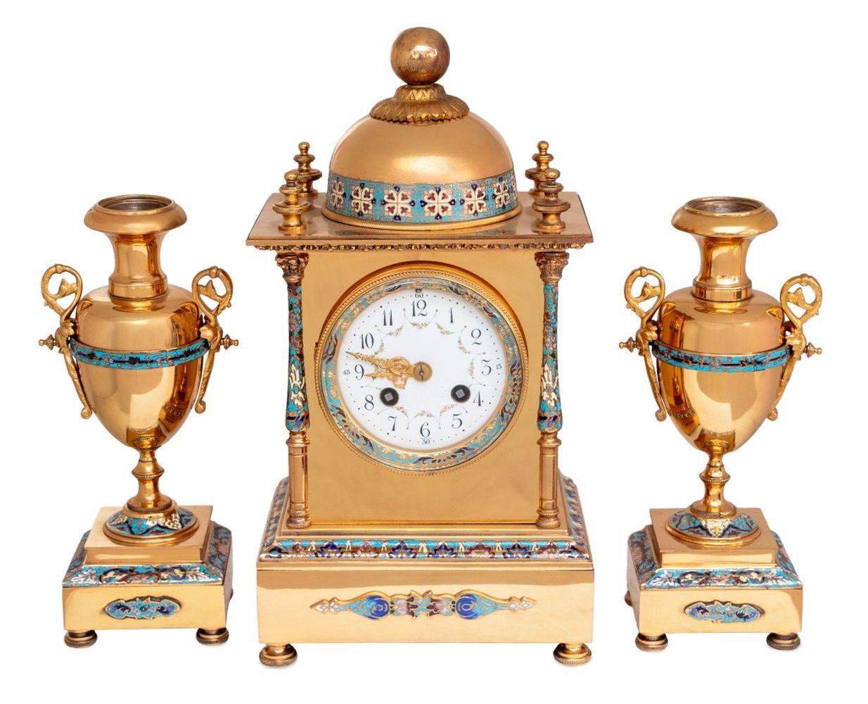 French Polished Brass and Champleve Enamel Clock Three Piece Clock Set, early 20th century, comprising: a clock surmounted by a dome, centered by a painted enamel dial, the movement strike on gong, flanked by balusters on a square plinth and pad