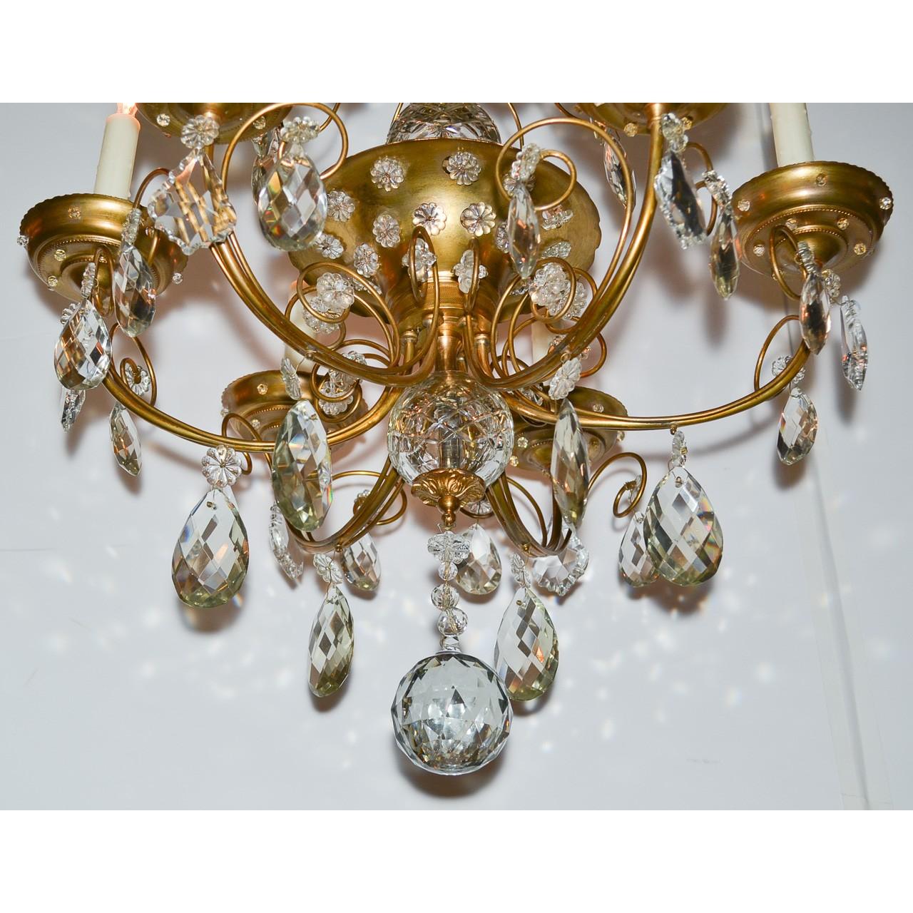 High style midcentury French brass and crystal chandelier, in the style of Maison Jansen. The fancy crystal spray crown above a small tier of crystal almond drops and a brass flared-mouth midsection mounted with scrolling arms decorated with faceted