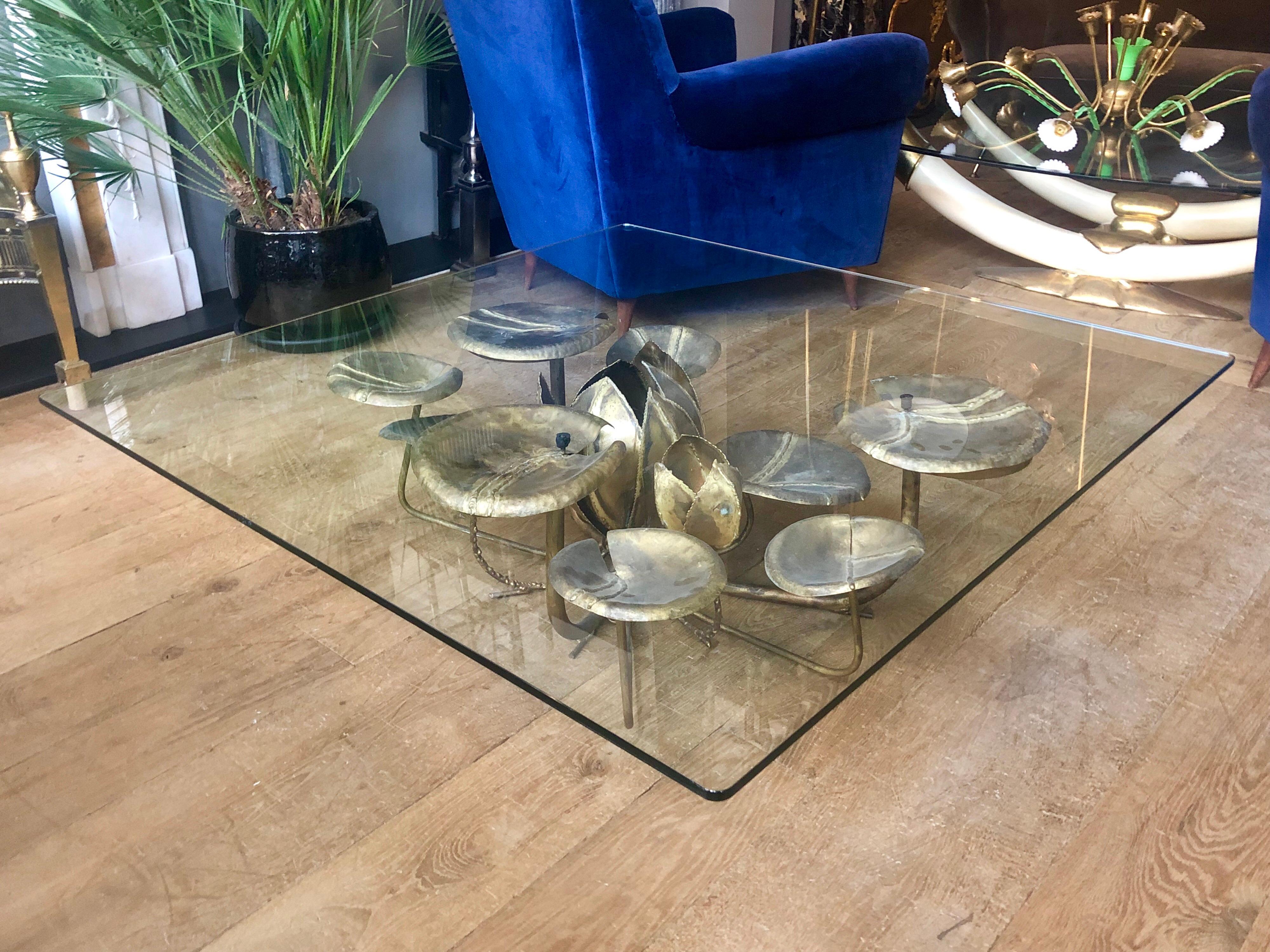 A large low cocktail table with a square glass top, supported by a base of Lilies with the central lily being lit. In brass and gold gilt iron, French, circa 1970s, by Maison Honore.
