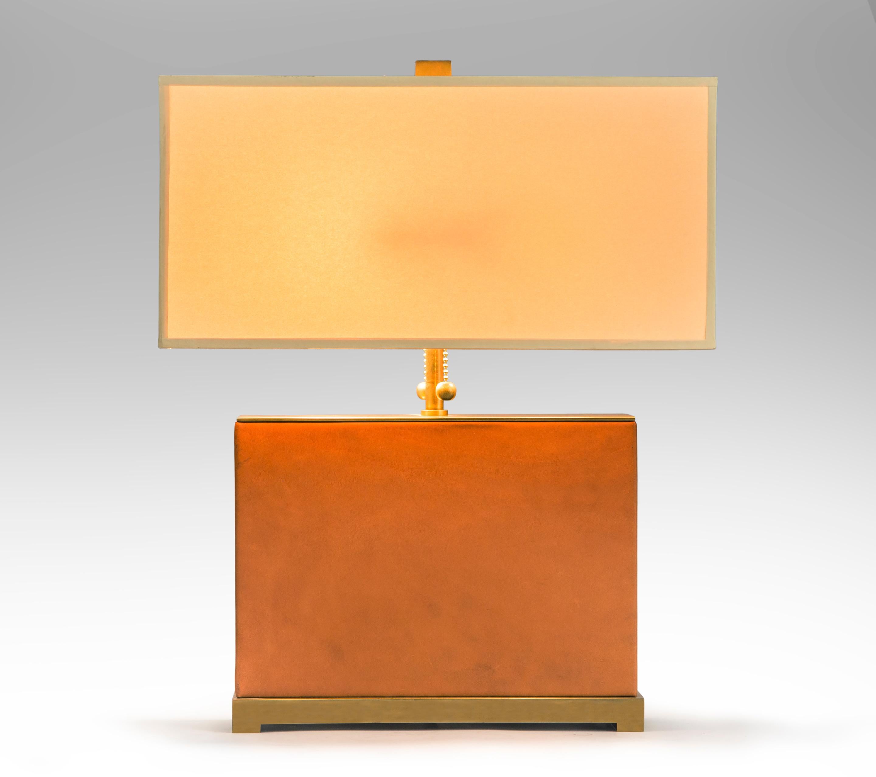 Brass and leather lamp,
late 20th century.
A discretely beautiful lamp crafted with skill and luxurious materials. The rectangular leather center raised on a footed brass platform, rectangular shade included. UL listed.