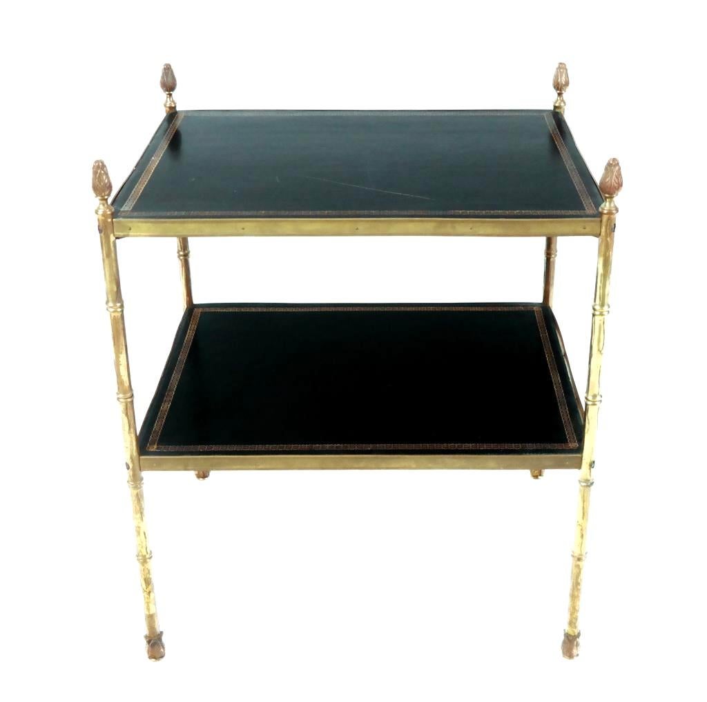 Table d'appoint en laiton et cuir estampé de la Maison Maison Jansen. La table rectangulaire est dotée d'inserts en cuir sur les deux étagères et d'épis de faîtage en forme de gland. Les quatre épis de faîtage en forme de gland coiffent chacun des