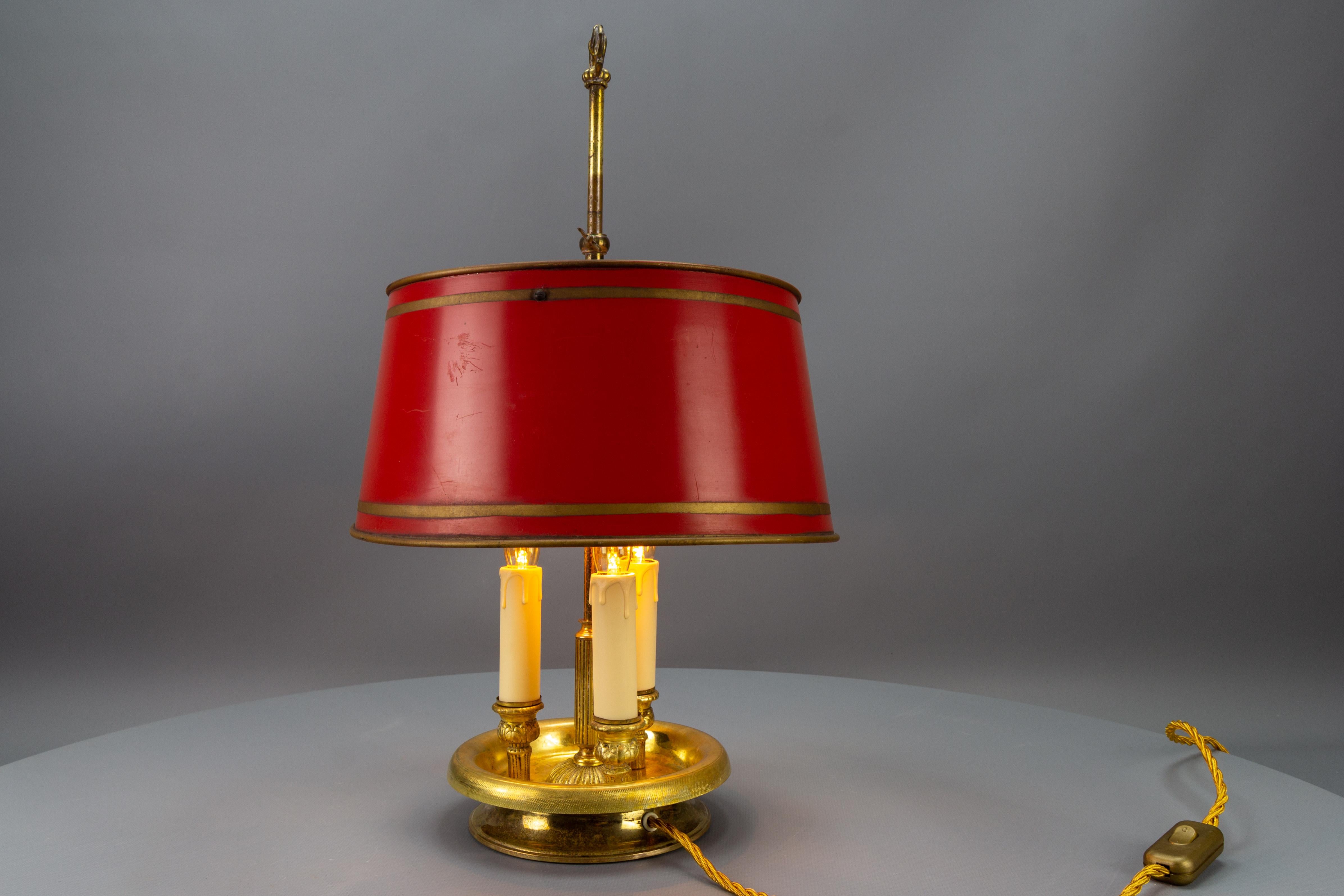 French brass and red tole shade three-light bouillotte desk or table lamp from circa 1950.
This beautiful three-arm / thre-light bouillotte table lamp features a fluted center column with an ornate base and an adjustable red-painted tole lampshade