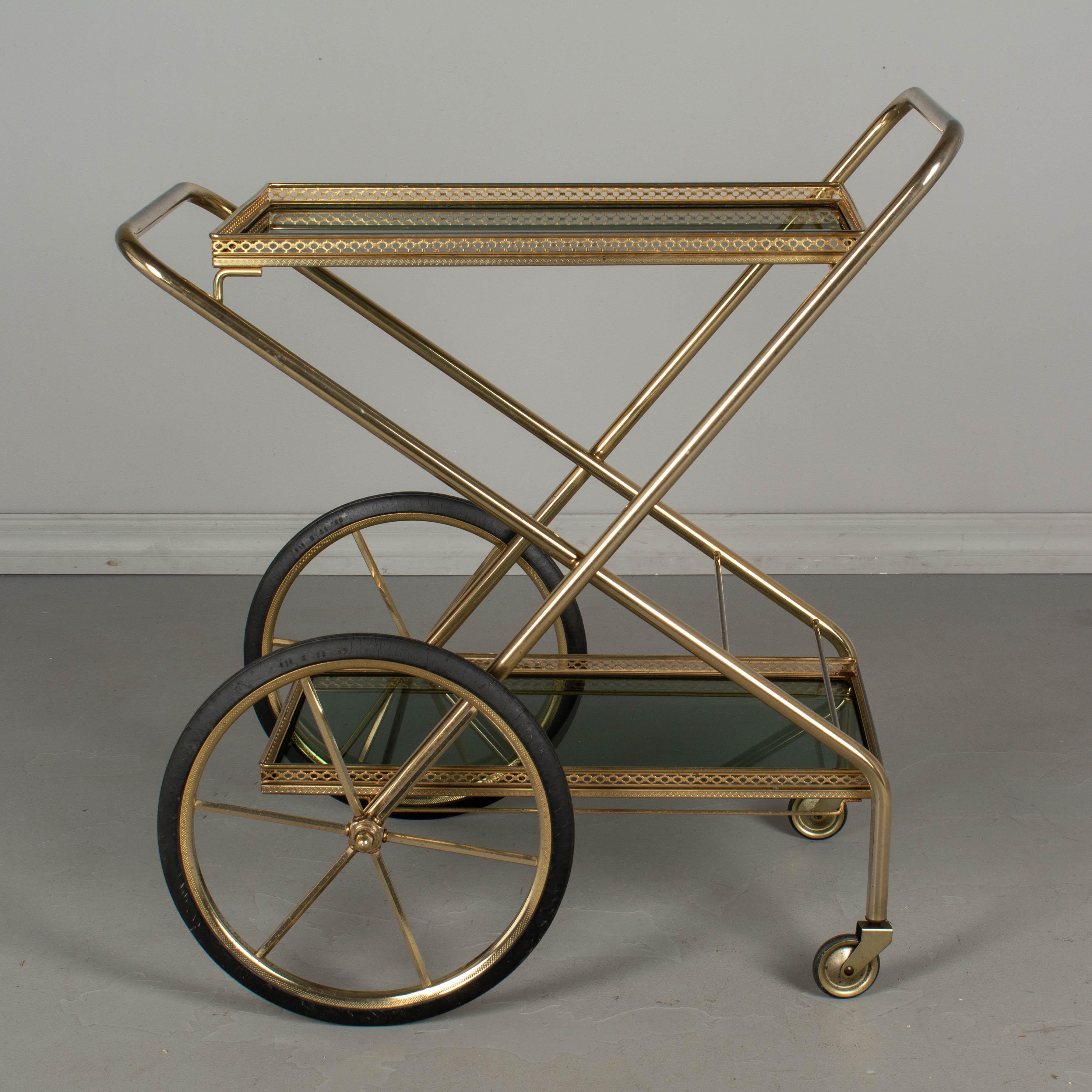 A French folding bar cart, or drinks trolley, with brass plated finish and smoke glass shelves with decorative gallery. The X-shaped frame is hinged and can be folded for easy storage. Superb design and well-made. Original rubber wheels glide