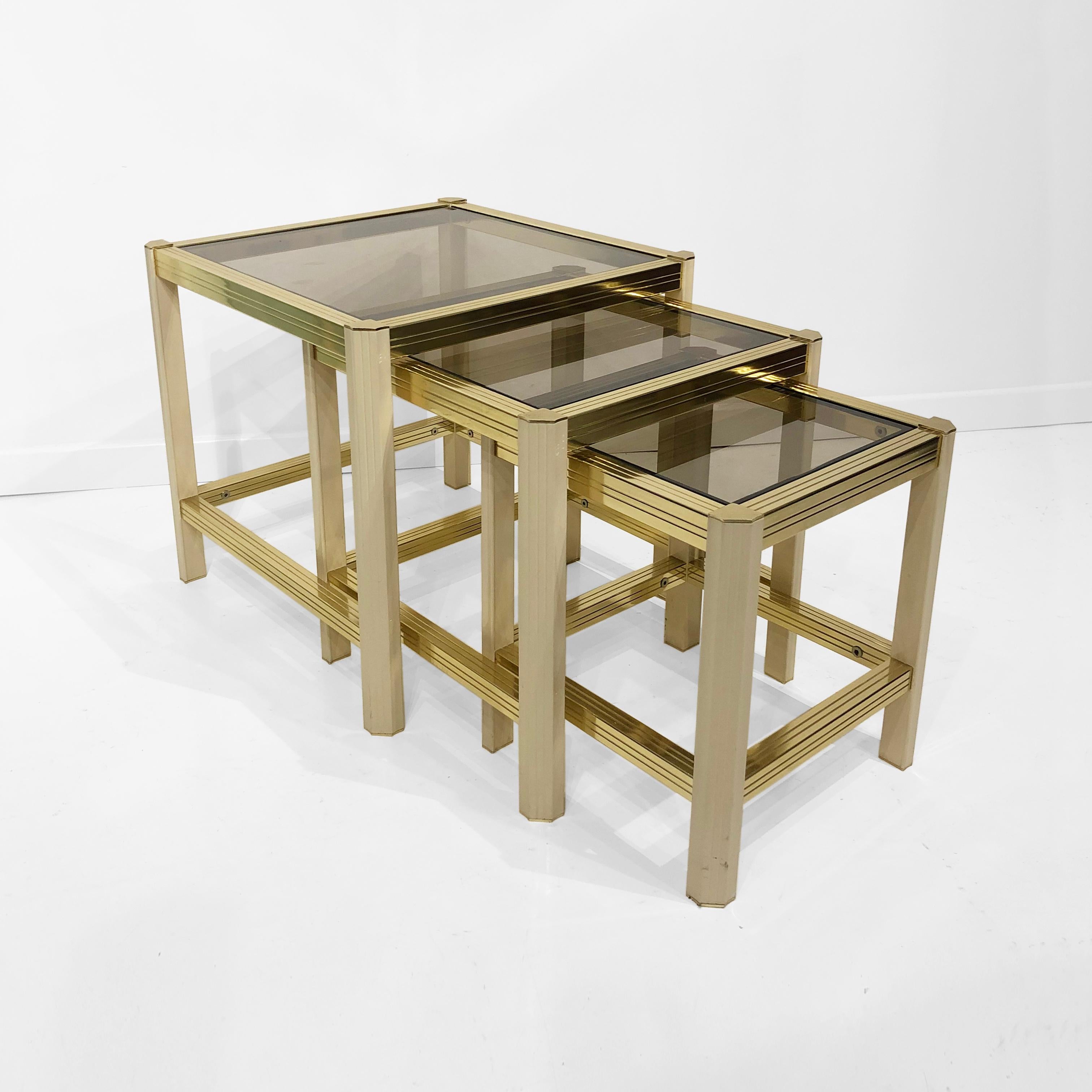 A trio of 1970s French nesting tables in a brass and cream-coated textured frame, with smoked glass tops. Each leg has a Pentagon shape with a light curve, and it is joined with the rigged brass plated bars. Very practical set of nest tables ideal