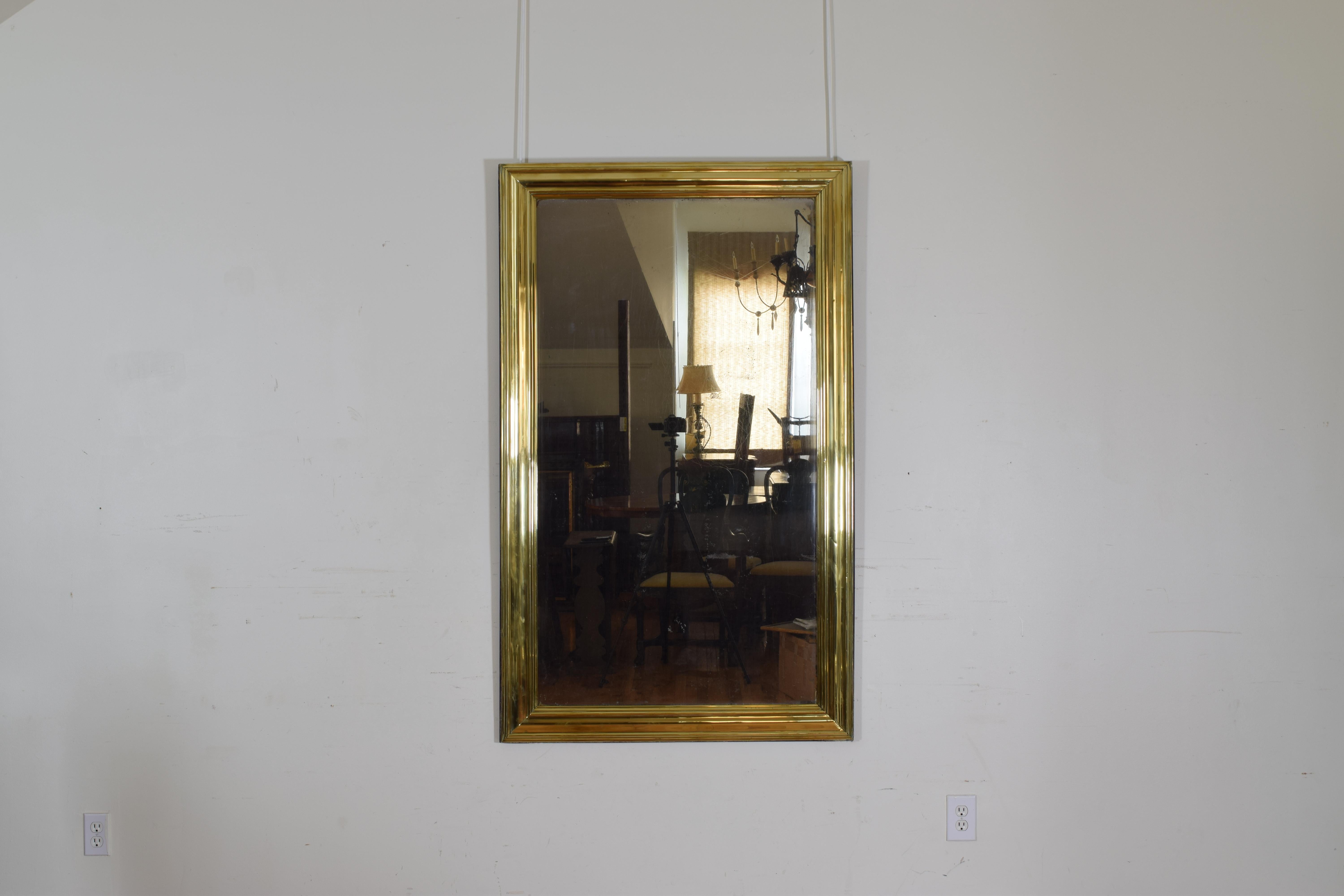 Shaped brass frame mounted atop a wooden backing, retaining antique mirrorplate.