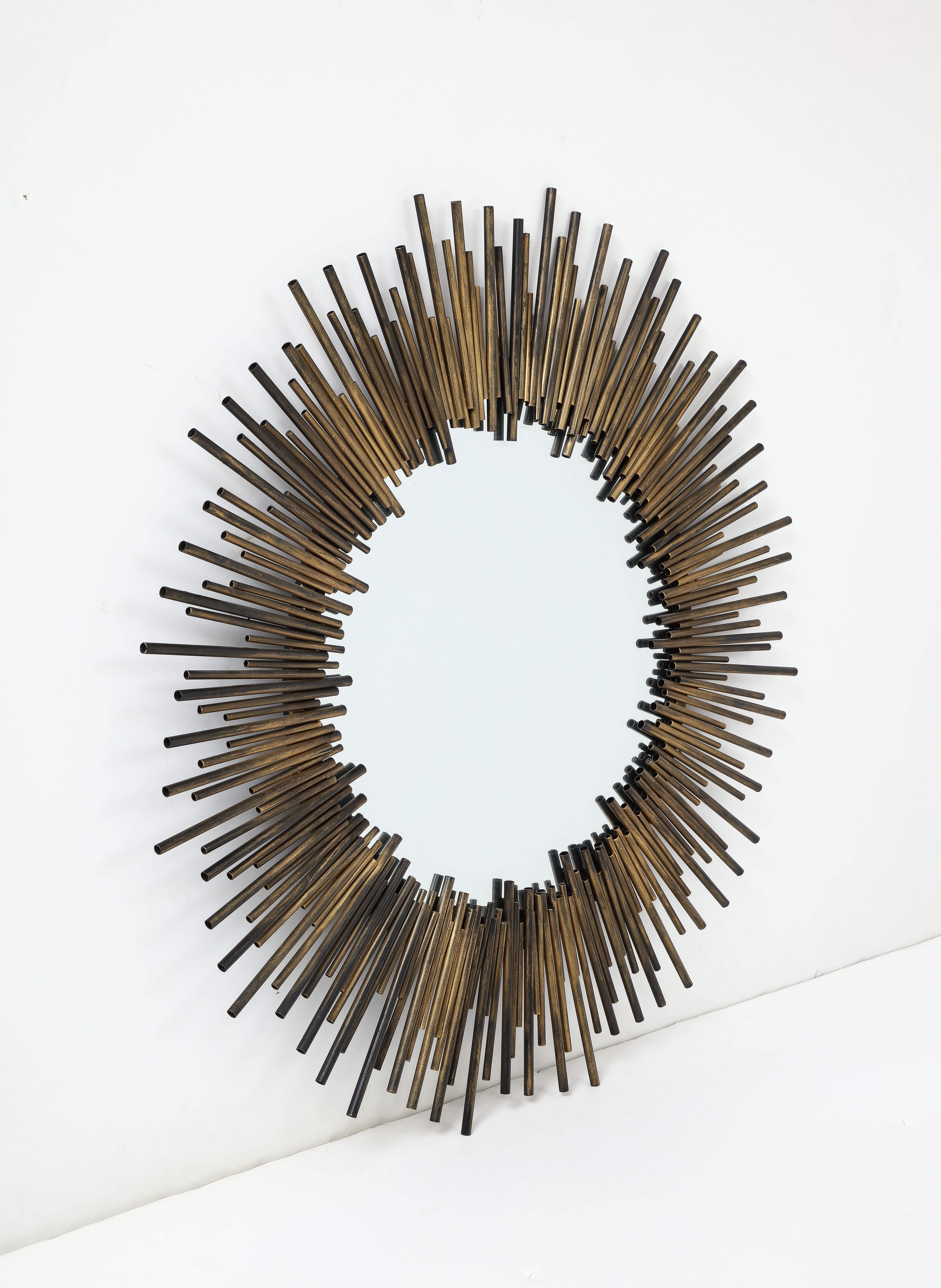 Modernist starburst mirror featuring a border made from hand welded brass and bronze tubes in varying lengths surrounding the center mirror panel.