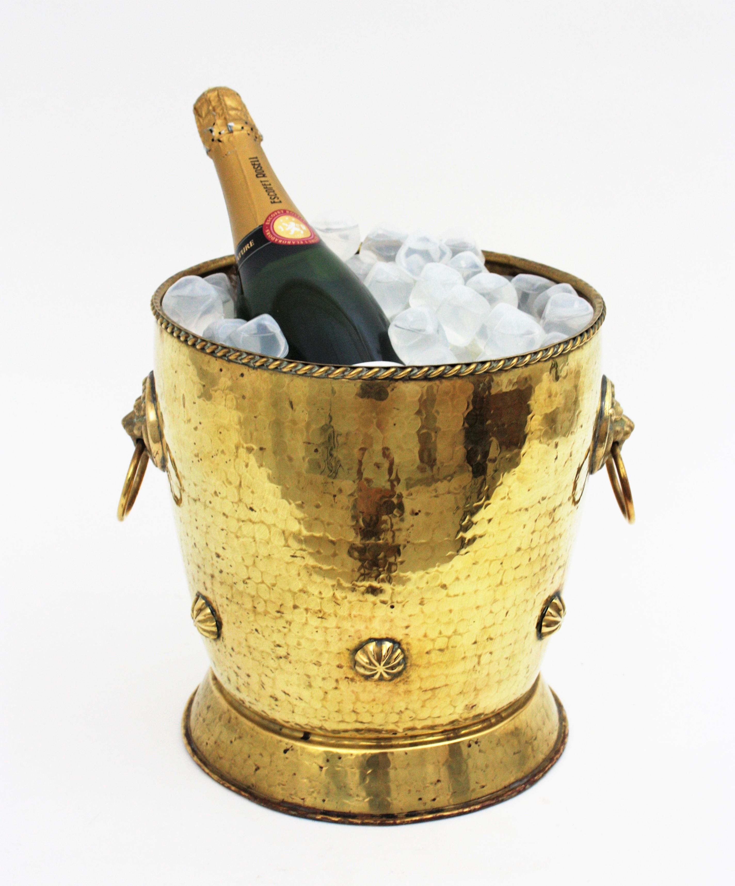 French brass ice bucket or wine / champagne cooler with lions head handles.
This hand-hammered brass cauldron is adorned by brass studs and it has a nice patina. At both sides it has lion heads holding brass rings in their mouths that serve as
