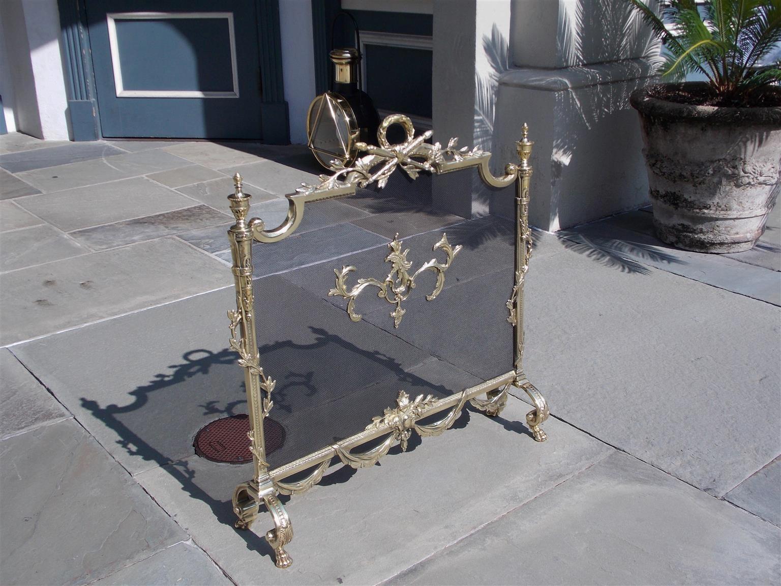 French brass decorative foliage and flanking urn finial free standing fireplace screen with centered laurel wreath torchere handle, flanking intertwined fluted floral side columns, lower connecting swags, and resting on the original scrolled fluted