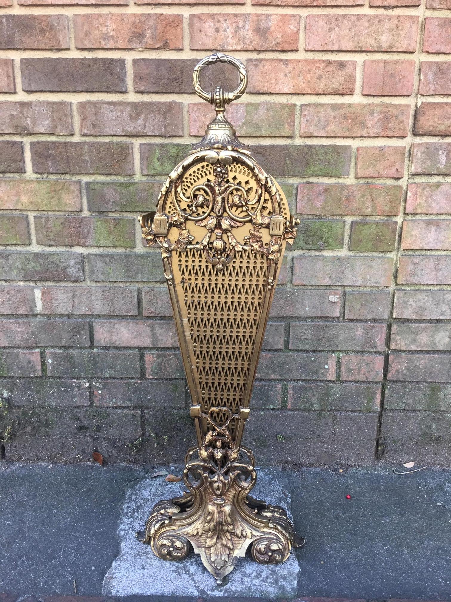 French brass decorative pierced folding fire place fan screen with a foliage and round handle, intertwined scrolled floral swags with a floral medallion, centered supporting bead work, and resting on a step back foliage medallion, and fluted finial