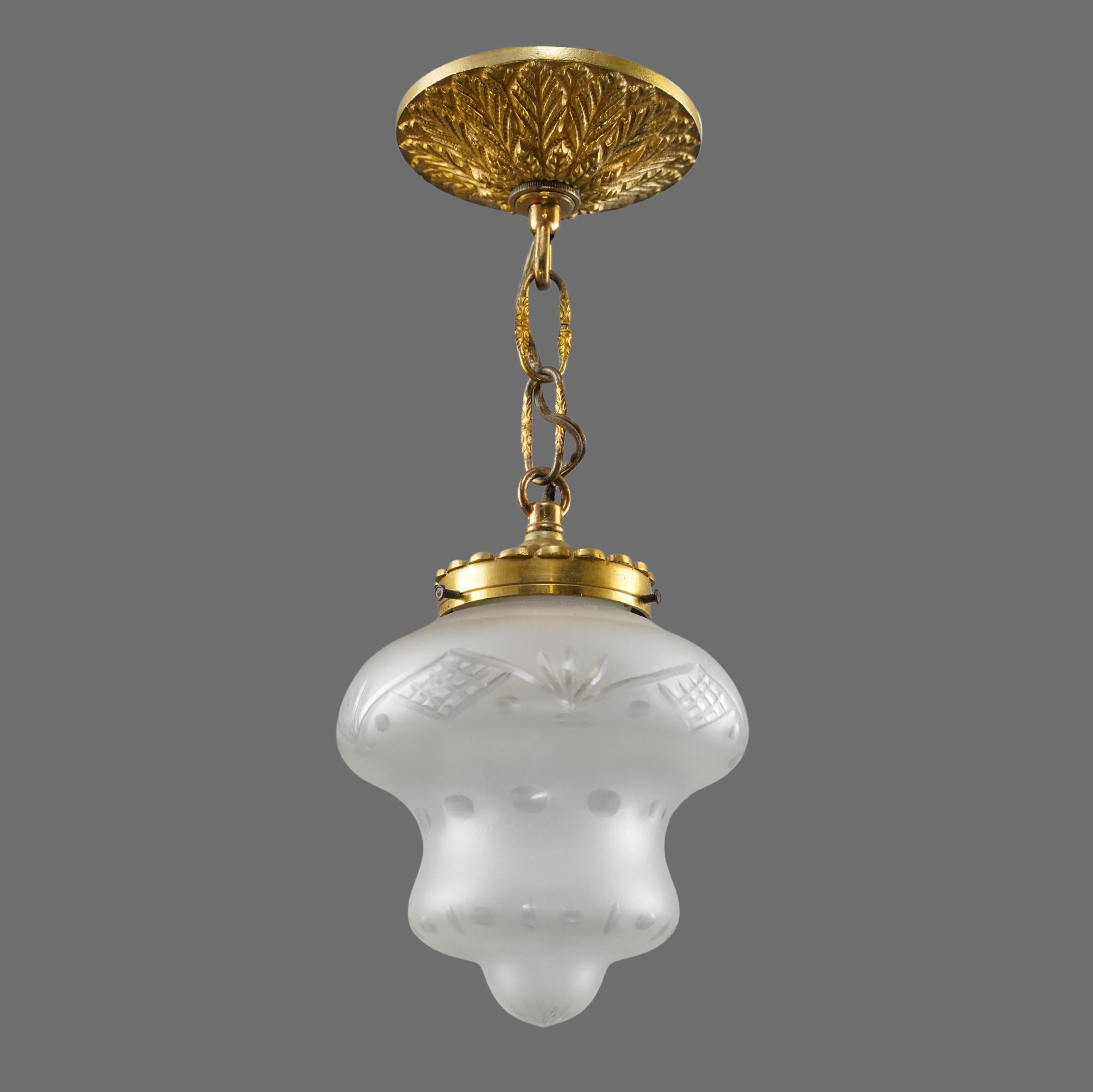 Lámpara colgante de estilo francés con un globo esmerilado y grabado con motivos geométricos y un enganche de cadena ornamentado de latón con acabado dorado. Requiere una bombilla estándar Edison de casquillo mediano. Limpiado y restaurado. Buen