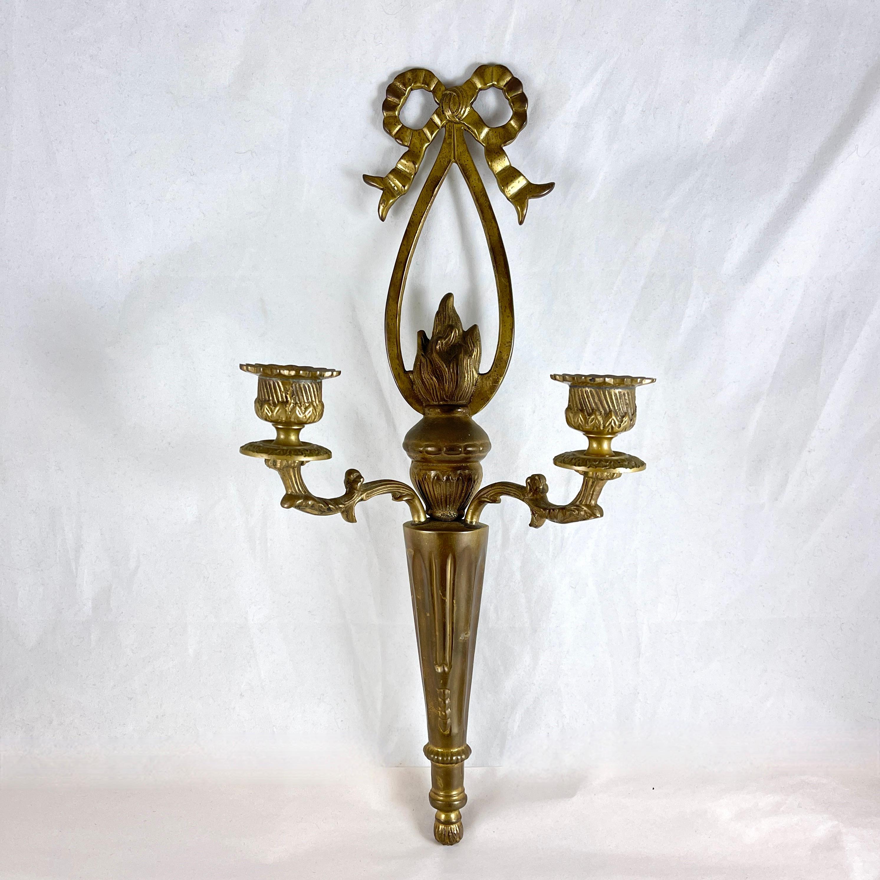 Aplique de latón con motivo de llama y lazo, Francia, hacia principios del siglo XX.

El candelabro de dos brazos está fundido en bronce pesado, con un lazo para colgar incorporado en el verso.

Forma de columna neoclásica con una llama encendida en