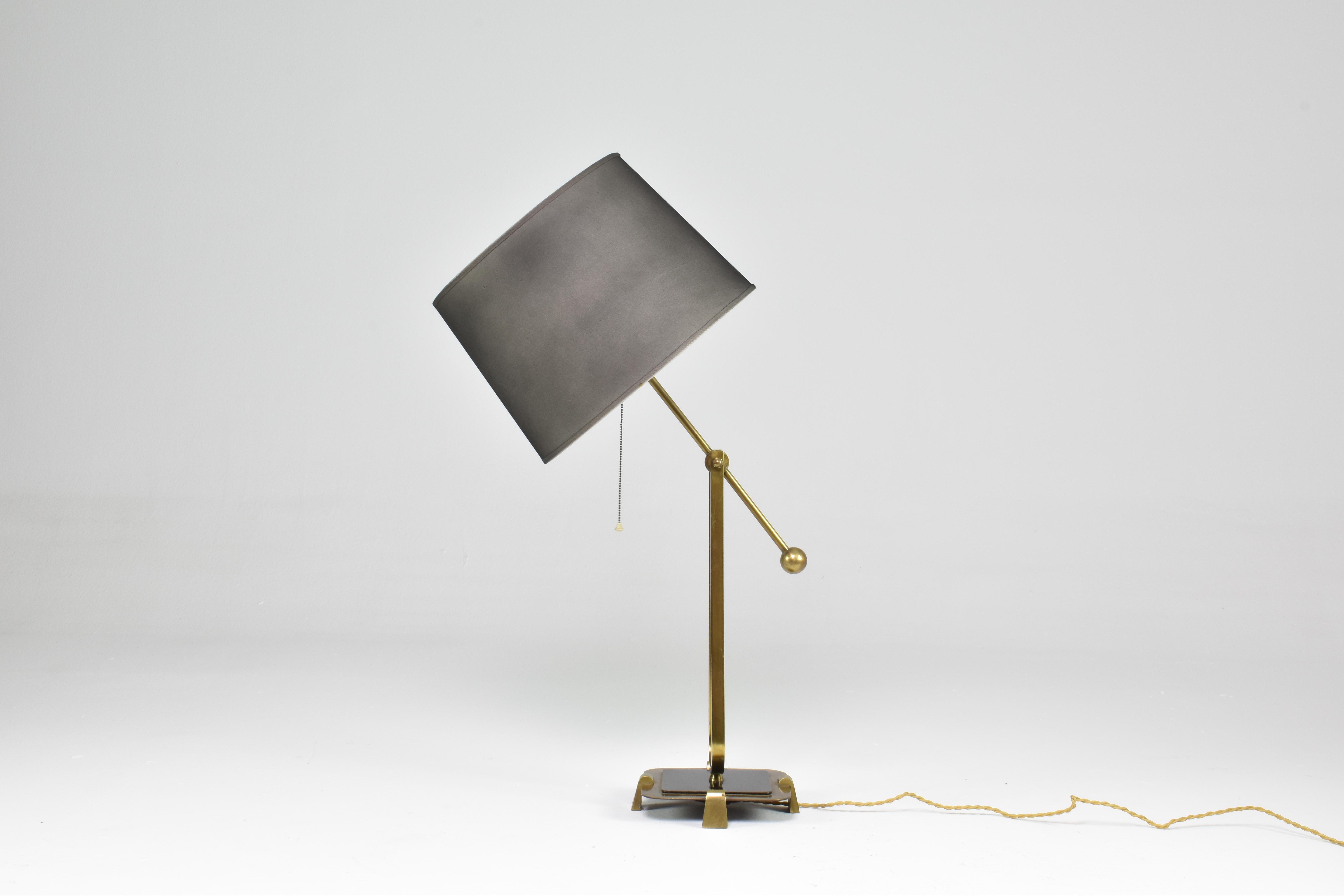 Une brillante lampe de table en laiton massif avec un interrupteur à chaîne en état entièrement restauré avec un nouvel abat-jour cylindrique. 
Le luminaire est super original car il est conçu avec un bras sophistiqué qui s'ajuste en hauteur grâce à