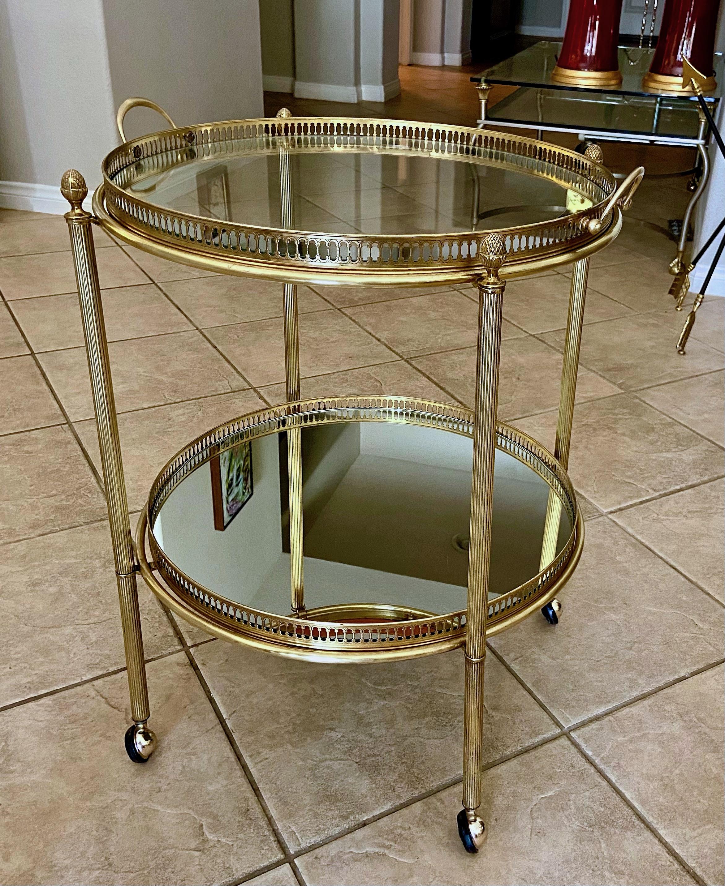 French brass round bar or tea cart with reeded legs, decorative pierced gallery rails and pomegranate finials. The trays are removable, the bottom tray is has an inset mirrored glass, the top tray is mirrored edge with clear glass center.