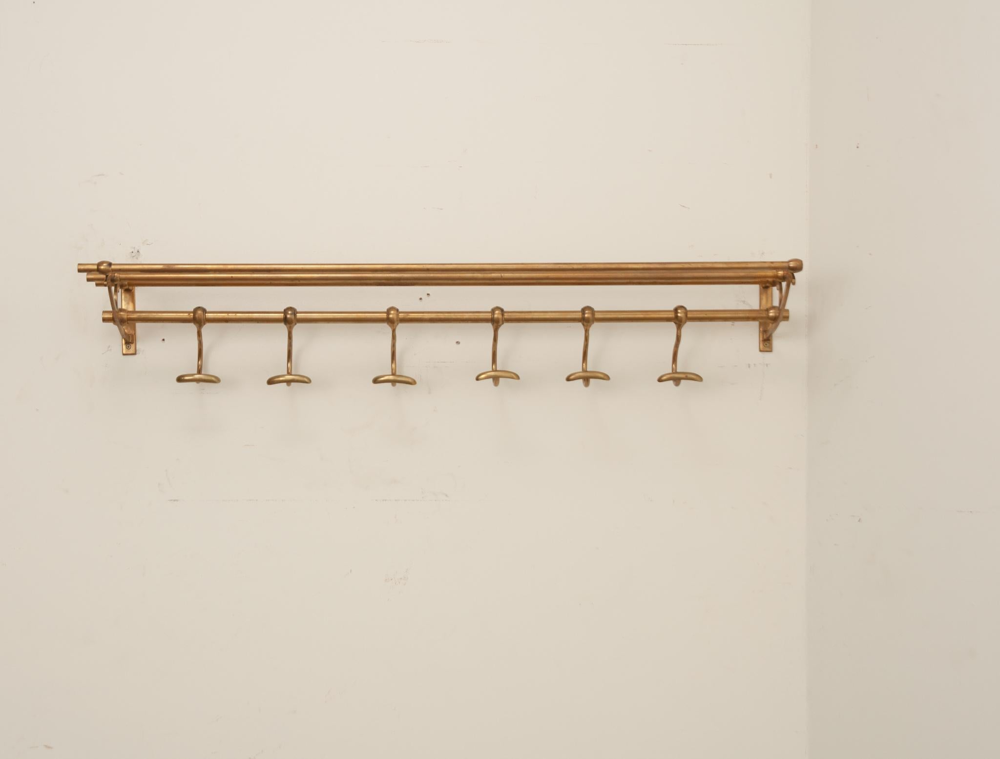 A French early 20th Century brass train rack is the perfect shelf by your door or in your bathroom. The 11 1/2” top shelf is deep enough for hats or towels. There are six slidable hooks for hanging coats or towels. Be sure to view the detailed