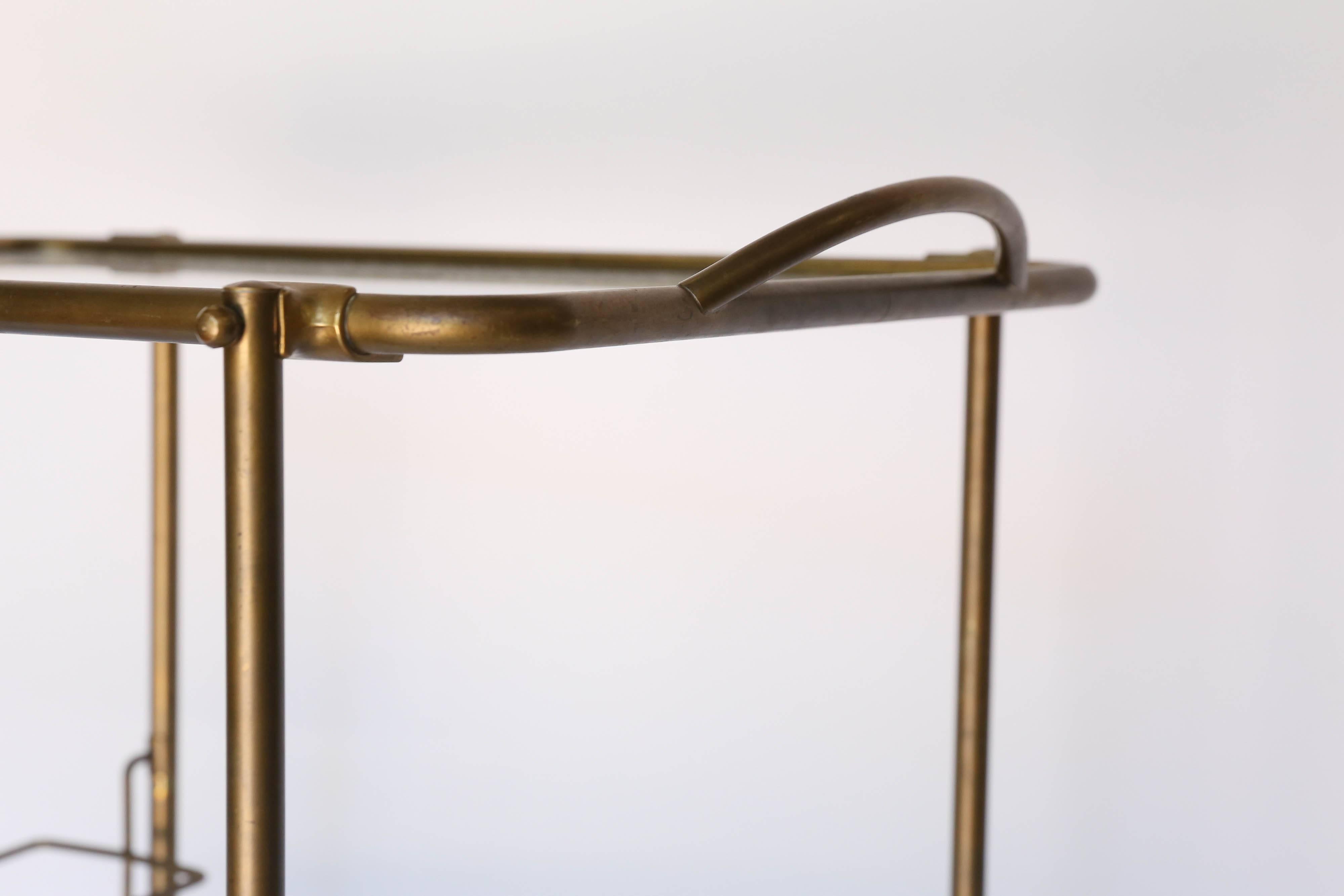 A French brass bar cart constructed with two levels of glass shelves with brass handle and wheels for easy transport. Display your vintage glassware, or serve your favorite cocktails and desserts.