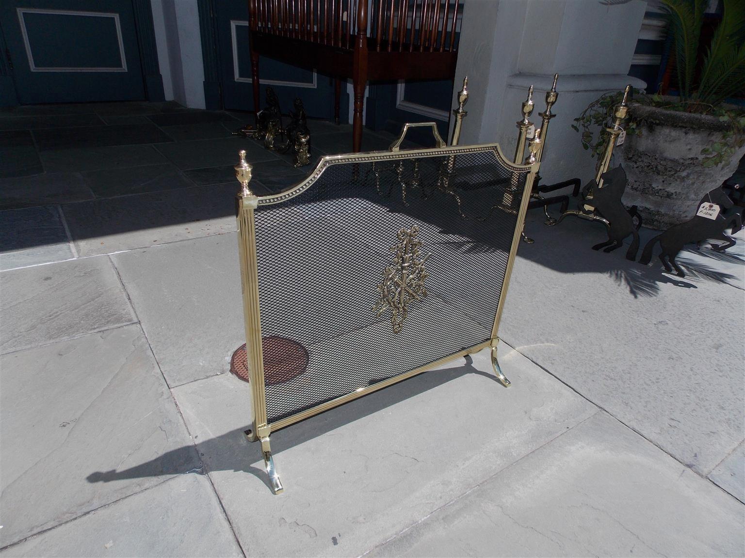 French brass free standing fire screen with flanking urn finials, centred upper handle, reeded and beaded border, centred decorative ribbon and floral motif, and terminating on the original scrolled feet. Late 19th century.