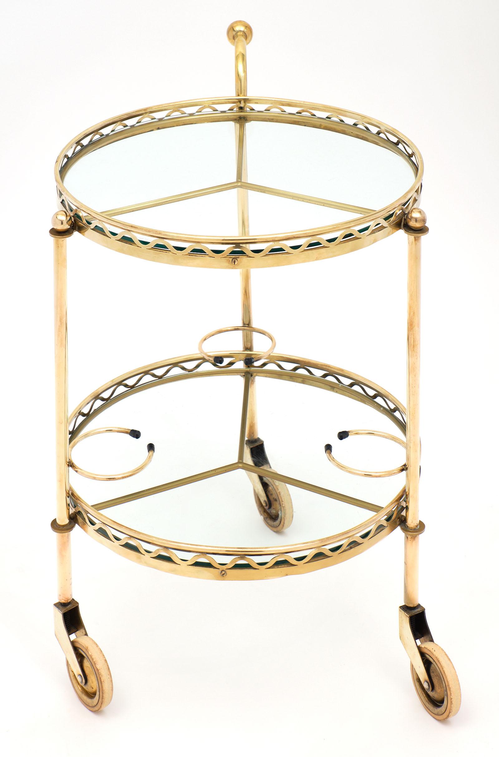 Vintage French brass bar cart with a fun, practical shape and gilt brass structure. The tripod casters are in excellent vintage condition and support two levels of clear glass. We love the bottle holders and the wave like decor on the trim.