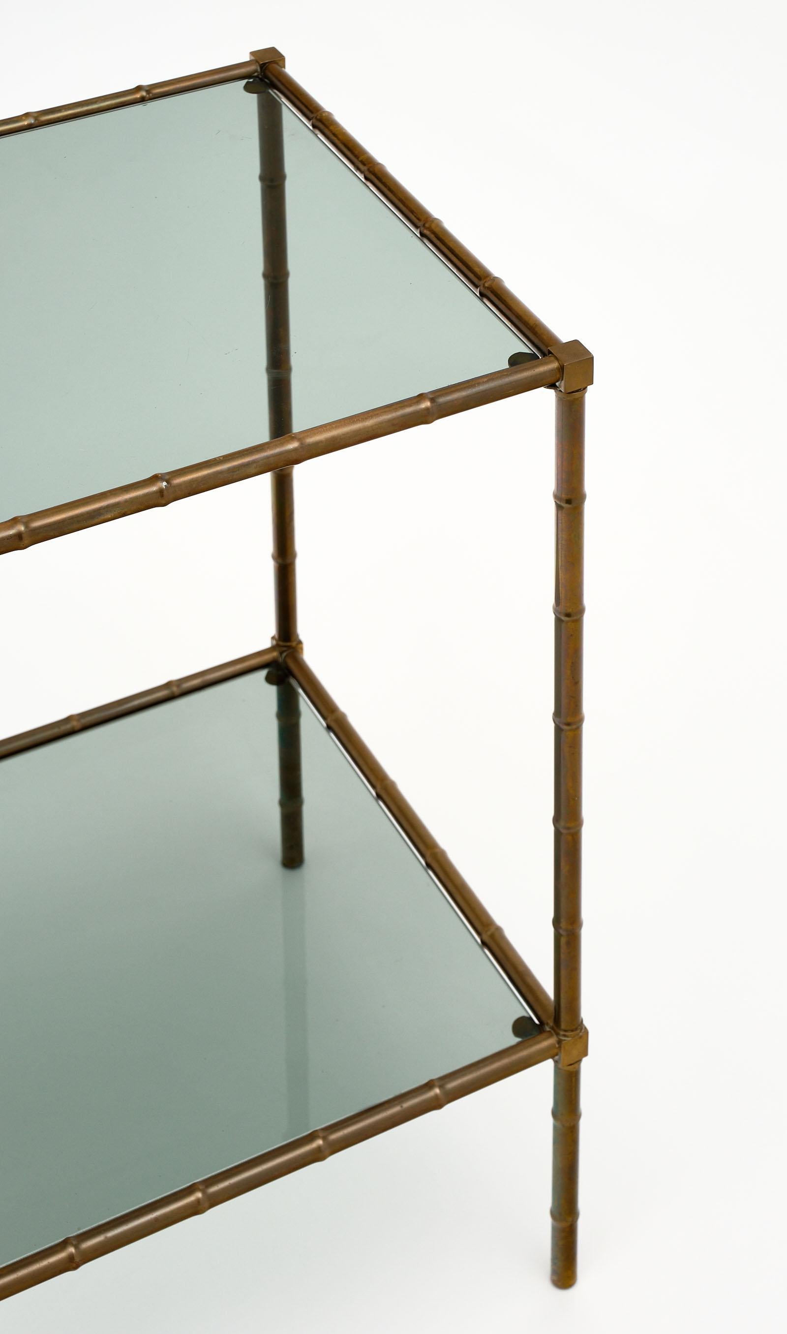 French brass vintage side table with two shelves of smoked glass. The brass frame with a beautiful patina boasts the stylized bamboo detail, attributed to Maison Baguès.