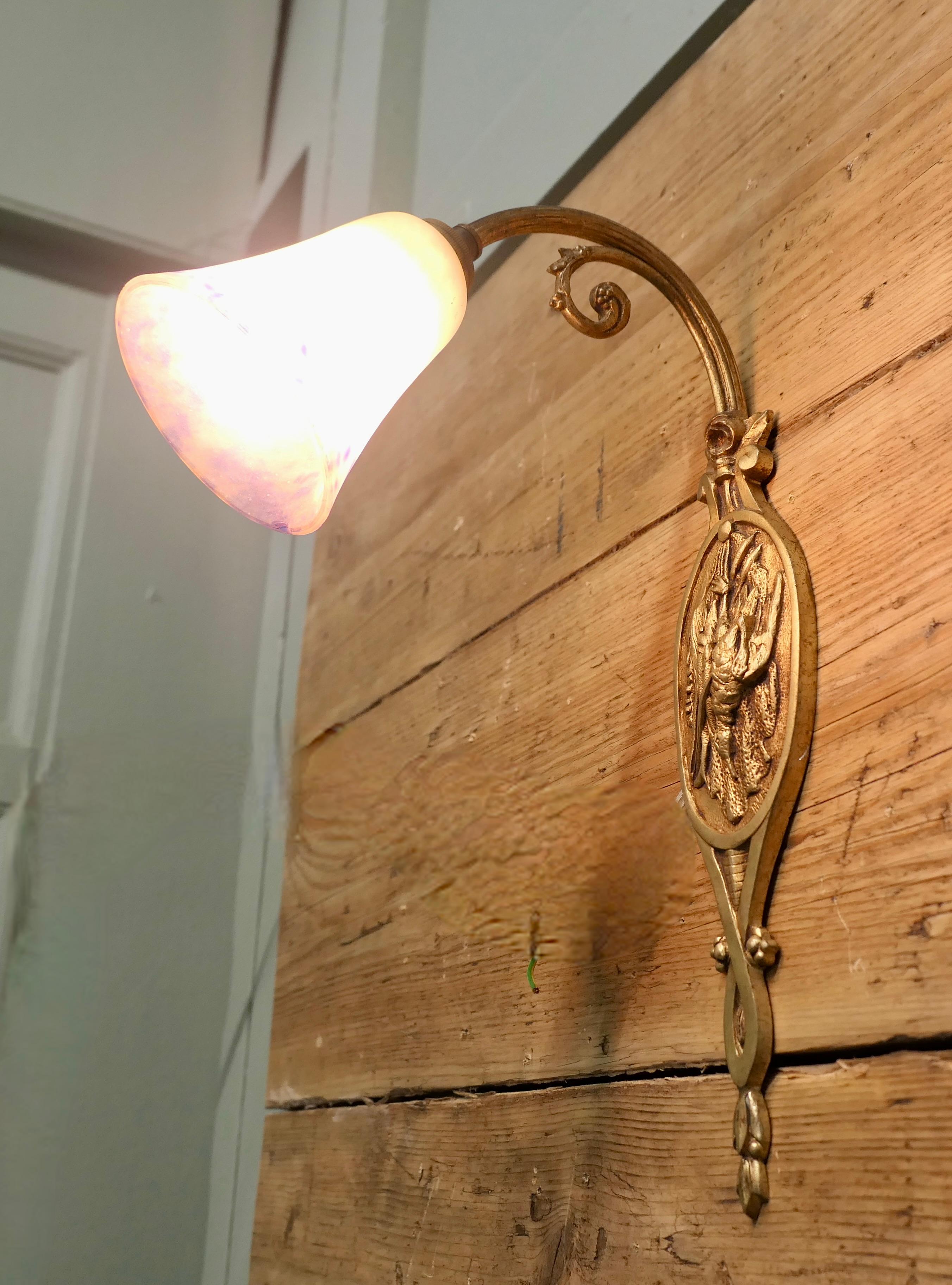French Brass Wall Light with Original Dugué Glass Shade

The Light has a brass swan neck arm and a back plate decorated with a hunting theme 
The Brass is darkened with age, the shade is original, it has a minute chip on the edge, this is so small