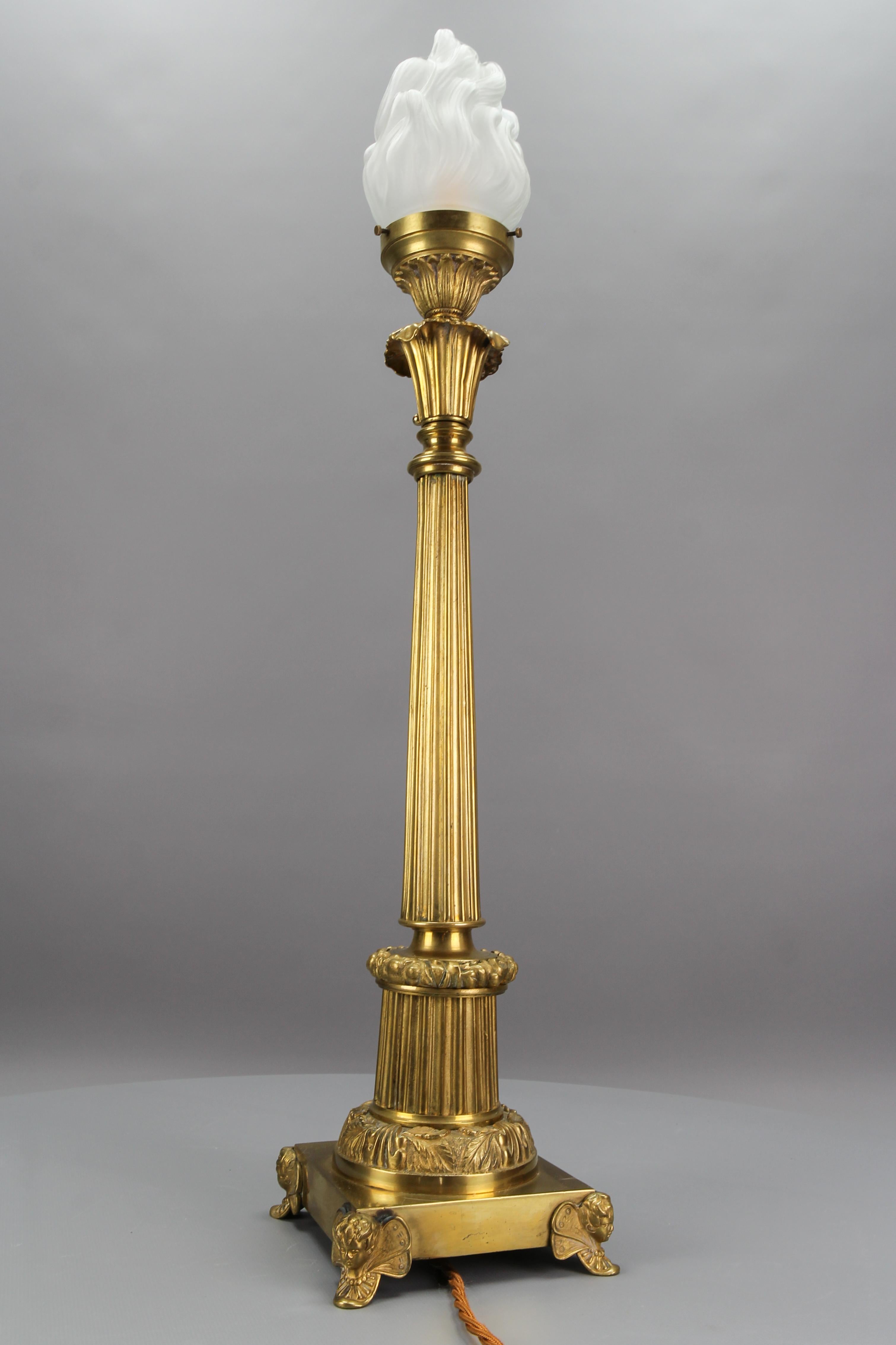 French bronze and frosted glass fluted column table lamp, circa the 1920s.
This impressive Art Deco period bronze lamp with a flame-shaped white frosted glass lampshade is standing on a square base supported by winged cupids on the edges, having a