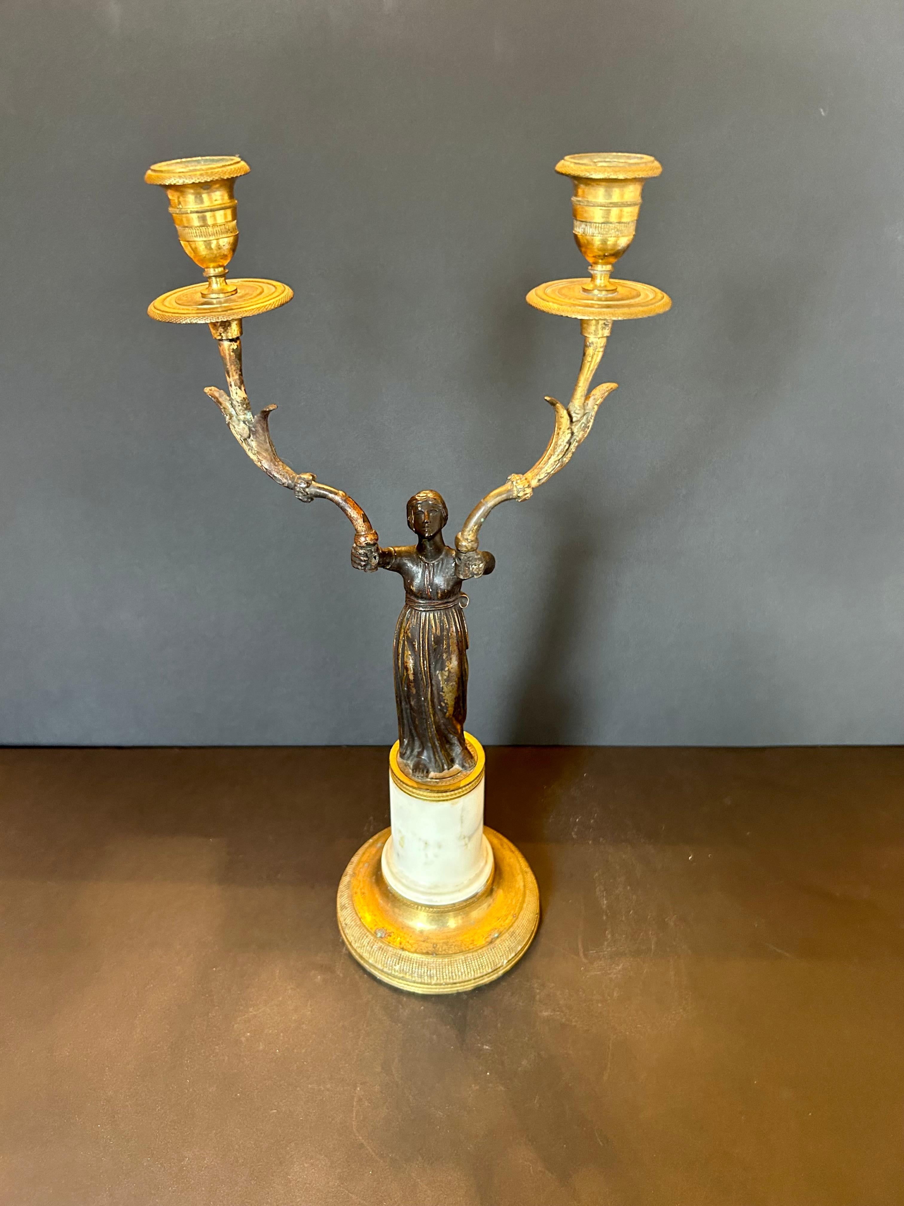 Un meraviglioso candelabro del XIX secolo in stile Impero francese, realizzato in bronzo patinato, bronzo dorato e marmo. Il gambo rappresenta una donna che tiene in alto una torcia a due braccia, il tutto poggiato su una base circolare in marmo