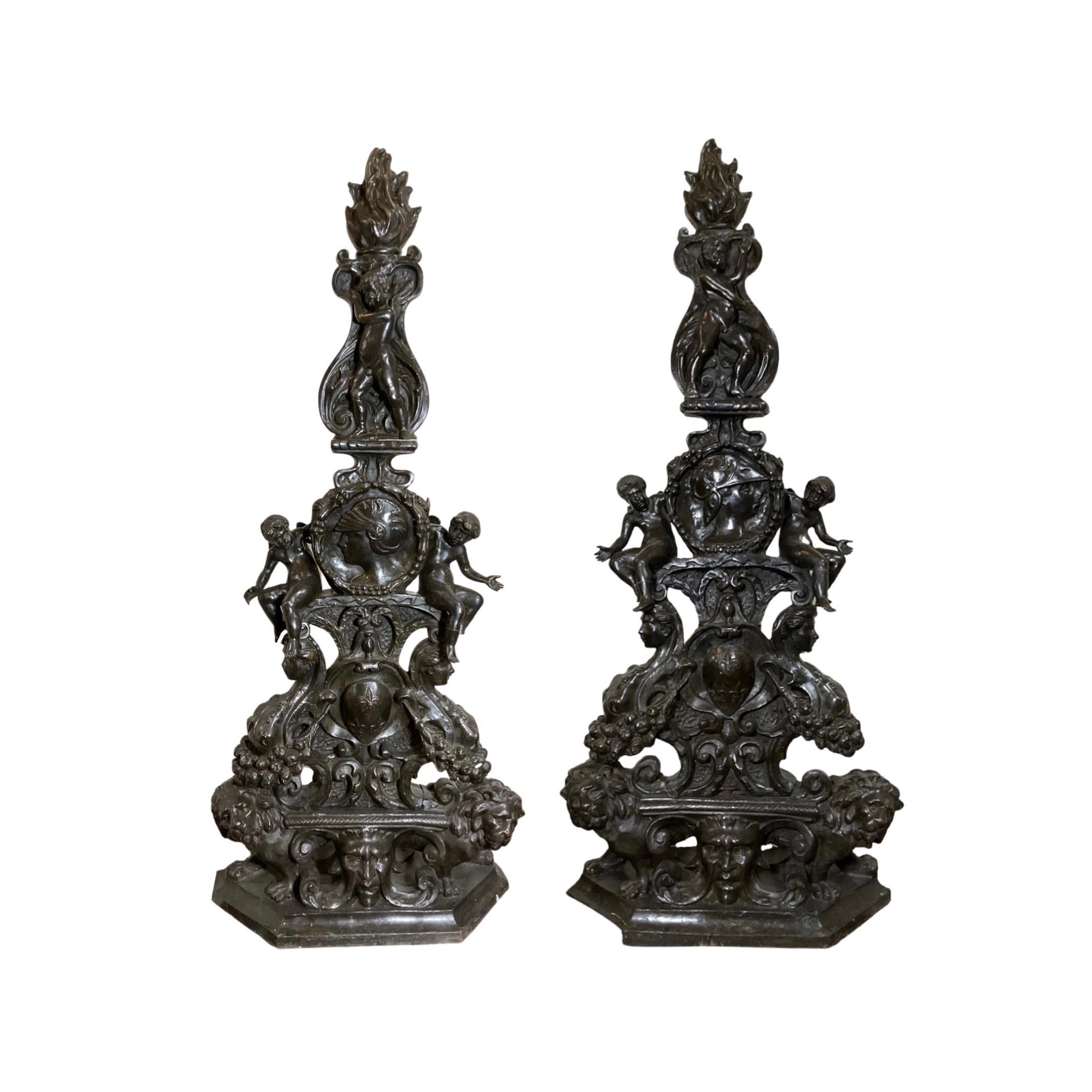 Diese sorgfältig gefertigten Chenets aus französischer Bronze und Eisen stammen aus der Zeit um 1790 und weisen entlang der Androns geschnitzte Puttenengel sowie Gesichtsdarstellungen auf. Dieses in Frankreich aus Bronze gefertigte Paar Chenets aus