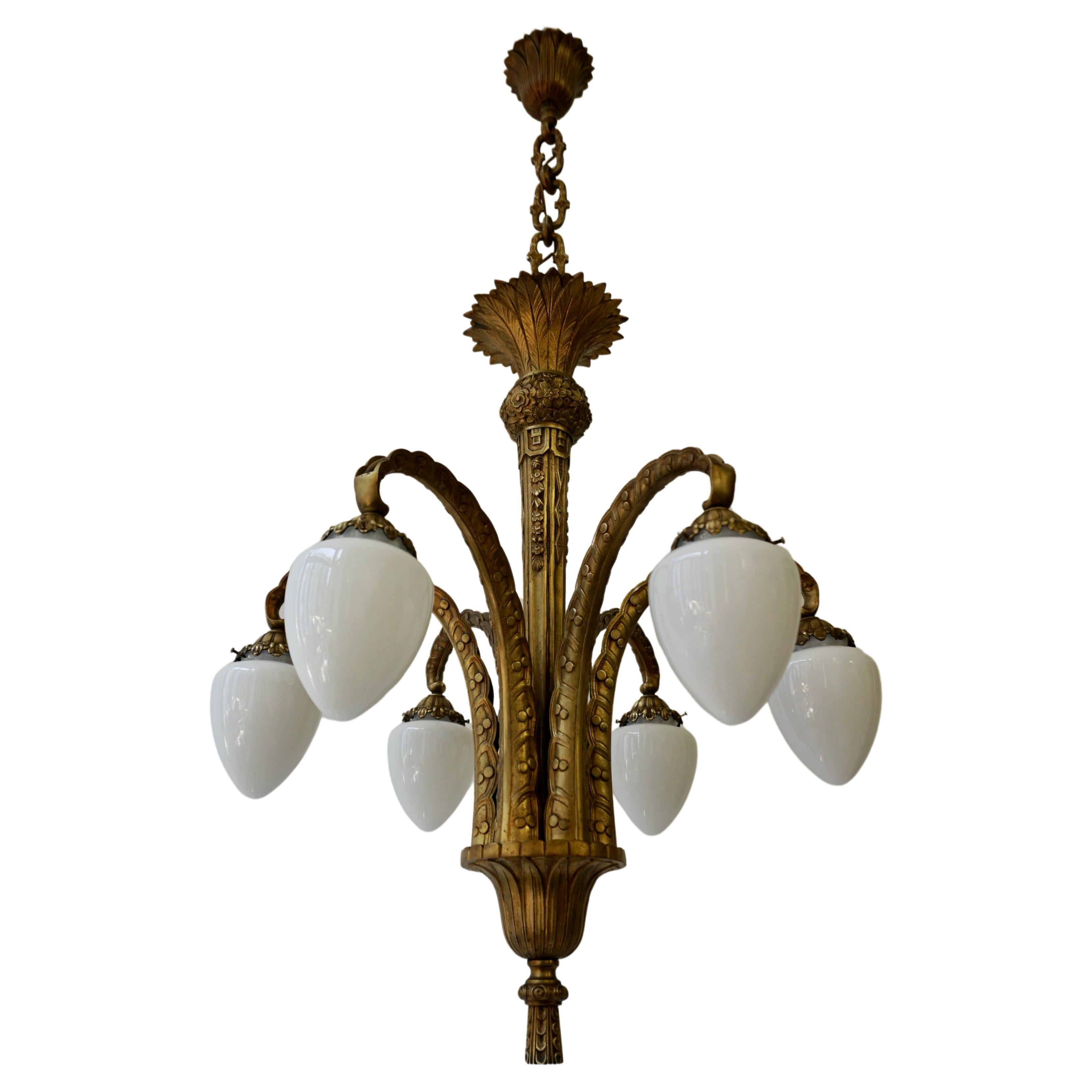 This unique French Art Deco bronze palm chandelier features a captivating and warm gilt bronze finish, with six flowing arms in a beautiful tropical arrangement. Each feather arm is decorated with beautifully shaped white opaline glasses. Adding to