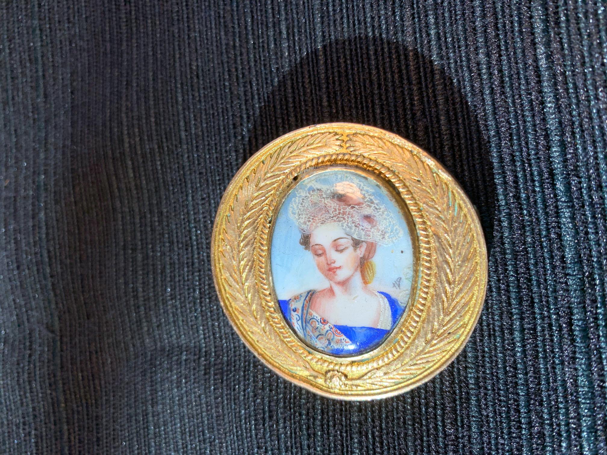 A cast bronze brooch by French Parisian Art Jeweler Line Vautrin (1913-1997) circa 1950s. The small lovely bronze pieces features a medallion insignia design with olive branch wreath surrounding an enamel portrait of a royal female, presumably Queen