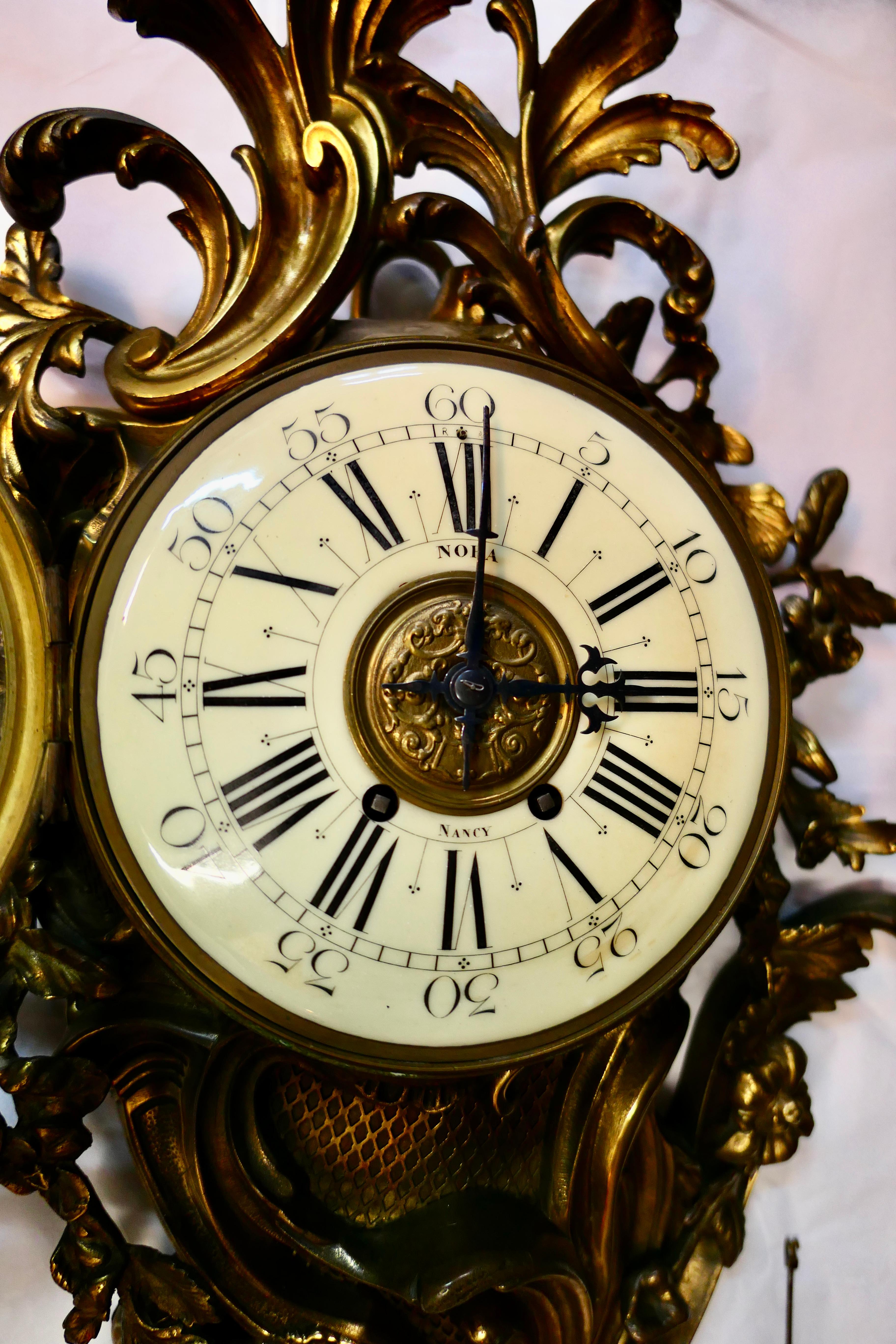 Cette horloge cartel (murale) française du milieu du 19e siècle de style Louis XV est magnifiquement conçue. Cette grande horloge en bronze sculpté est décorée de feuilles et de vignes florales qui dominent son apparence. Une face émaillée de