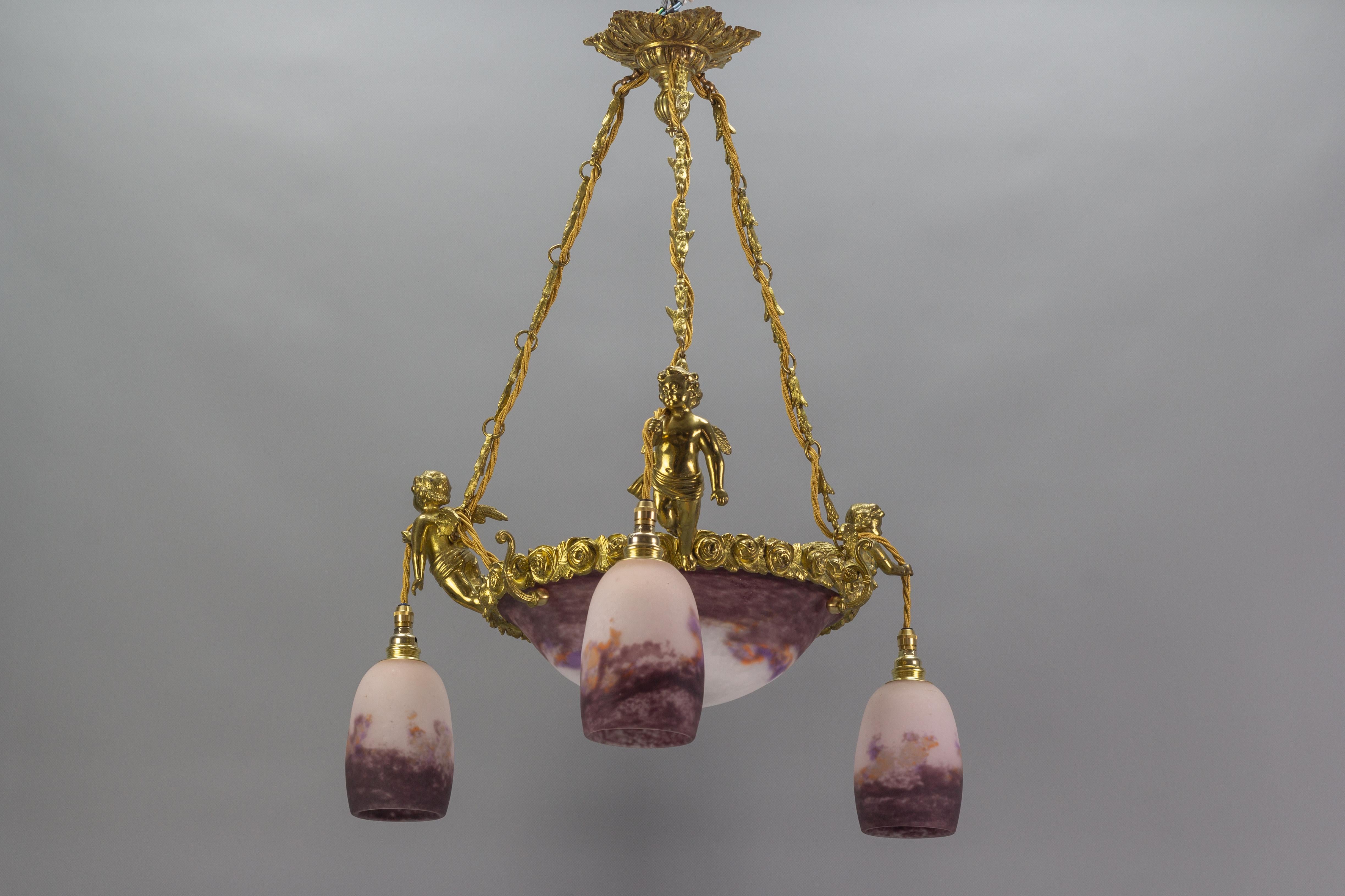 This absolutely delightful French Art Nouveau four-light chandelier features an ornate bronze fixture adorned with roses and three cherubs, each holding a light with a glass lampshade; and an interior light that brightens the beautiful dark violet,