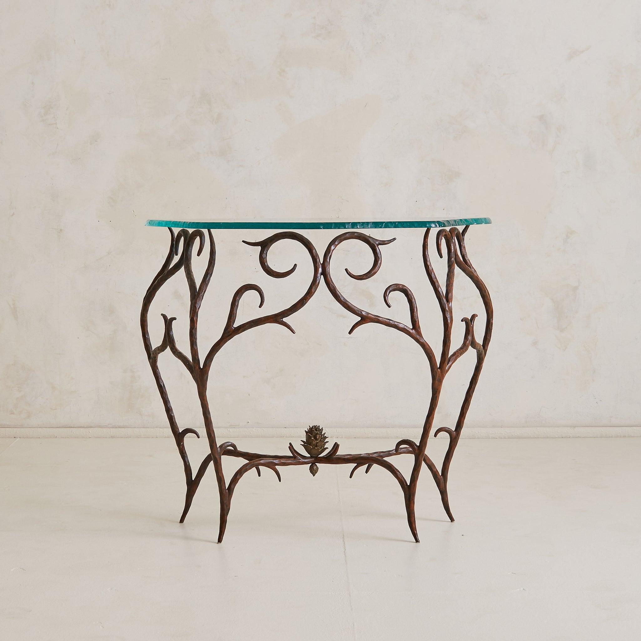 Console française lyrique des années 1970, fabriquée en bronze forgé à la main et dotée d'un plateau en verre ciselé. Le cadre se déploie en lignes sinueuses et en branches ramifiées, chacune martelée avec intention. À sa base, une pomme de pin en