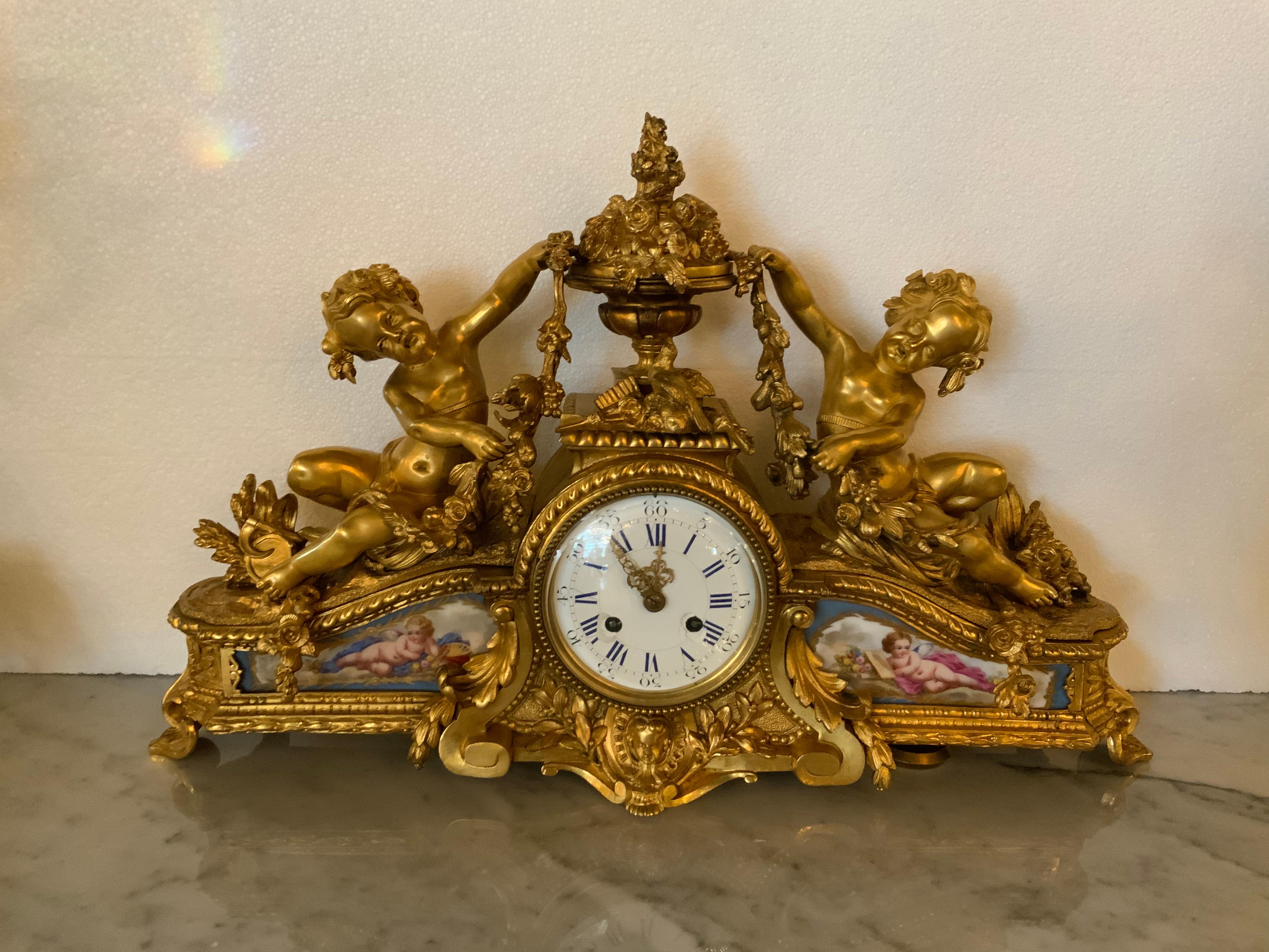 Bronze gilt French mantel clock with Sevres style porcelain painted with cherubs. A centered urn
At the crest with floral and foliate design. A petite bird centered at the top. Two gilt cherubs
Are at each side supporting garlands of flowers.