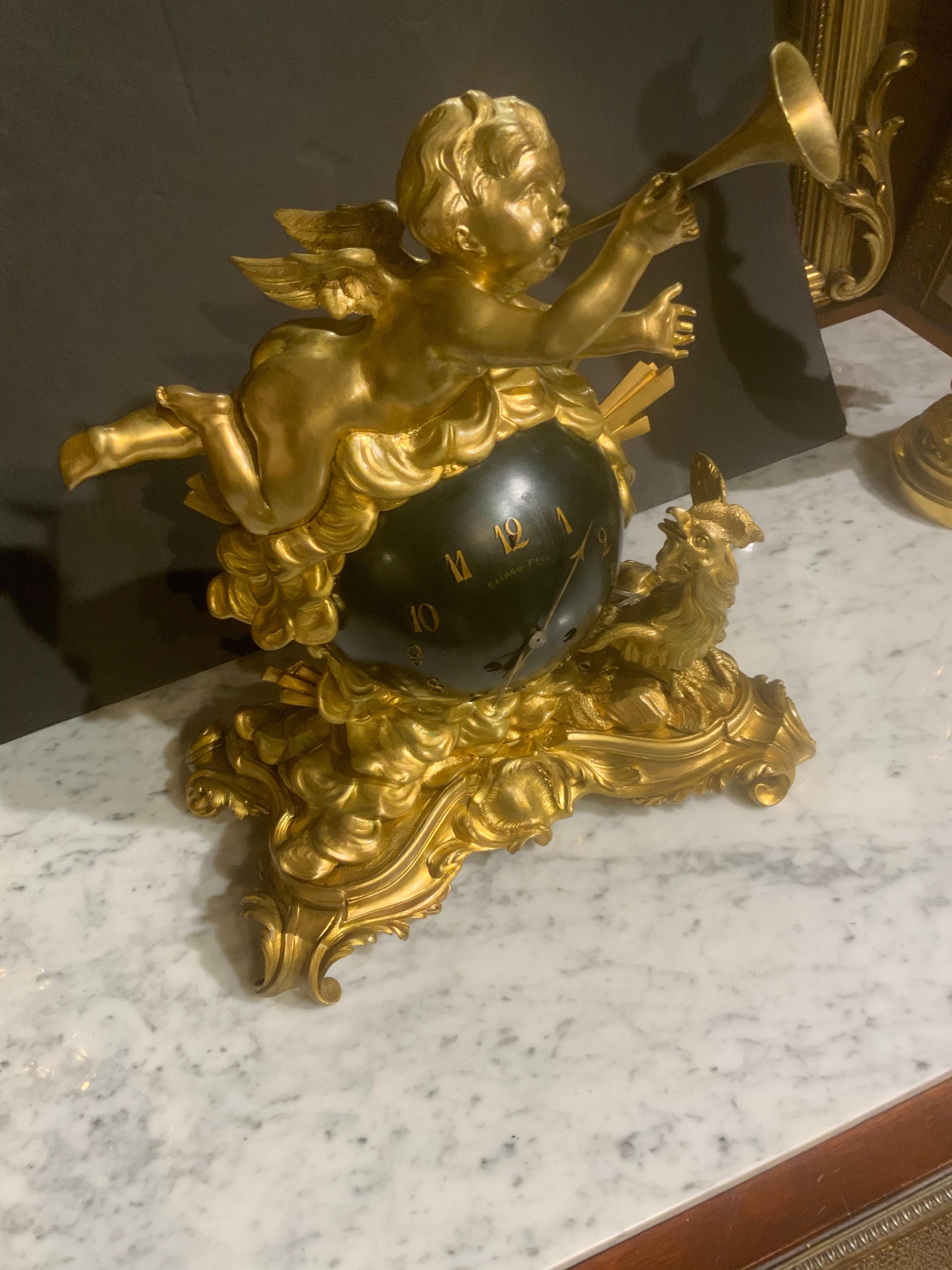 L'eccezionale qualità e la doratura rendono questo orologio speciale.
Il putti tiene in mano un corno che annuncia il nuovo giorno.
Anche il gallo alla base dà il benvenuto a un nuovo mattino.
La sfera nera rappresenta il globo terrestre e riporta