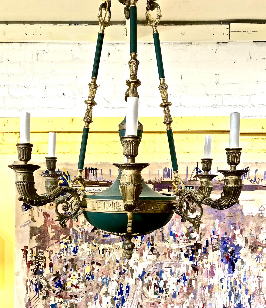 This is an early 20th century example of a Classic French Empire bronze chandelier. The French green tone of the painted metal contrasts beautifully with the dore bronze mounts and decorations. The chandelier is suspended on three bronze detailed