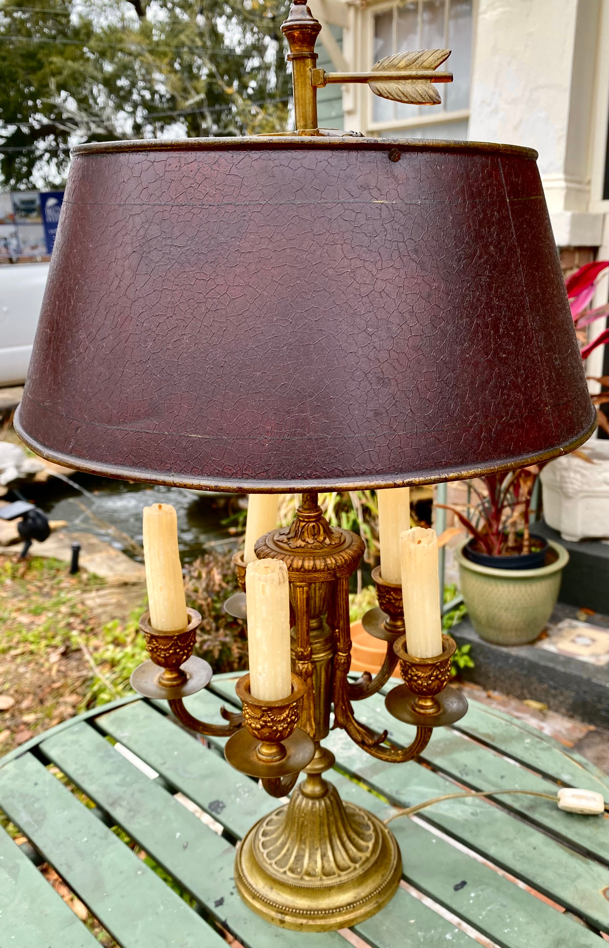 French Louie XVI style gilt bronze bouilotte table lamp featuring a tall, detailed cylindrical stem crowned by an arrow finial over a deep brown/burgundy tole conical shade concealing five S-form light sockets, followed by five foliat U-shaped