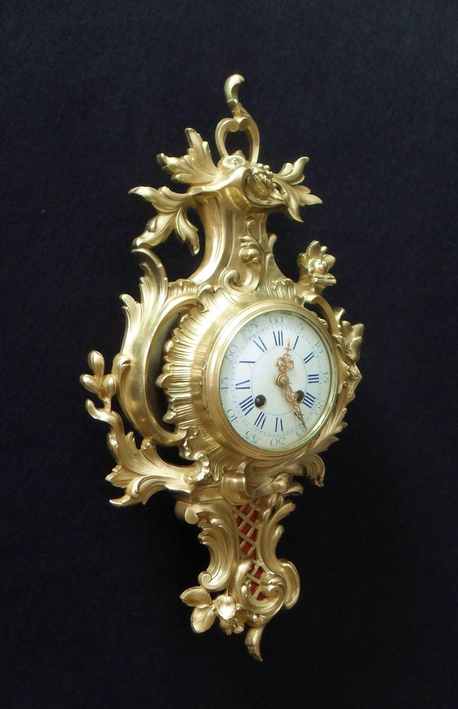 A decorative French bronze gilt ormolu Cartel wall clock in the Rococo style with floral and scrolling leaf design. The clock has a white enamel dial with roman numerals and a French eight day movement which strikes the hours and half hours on a