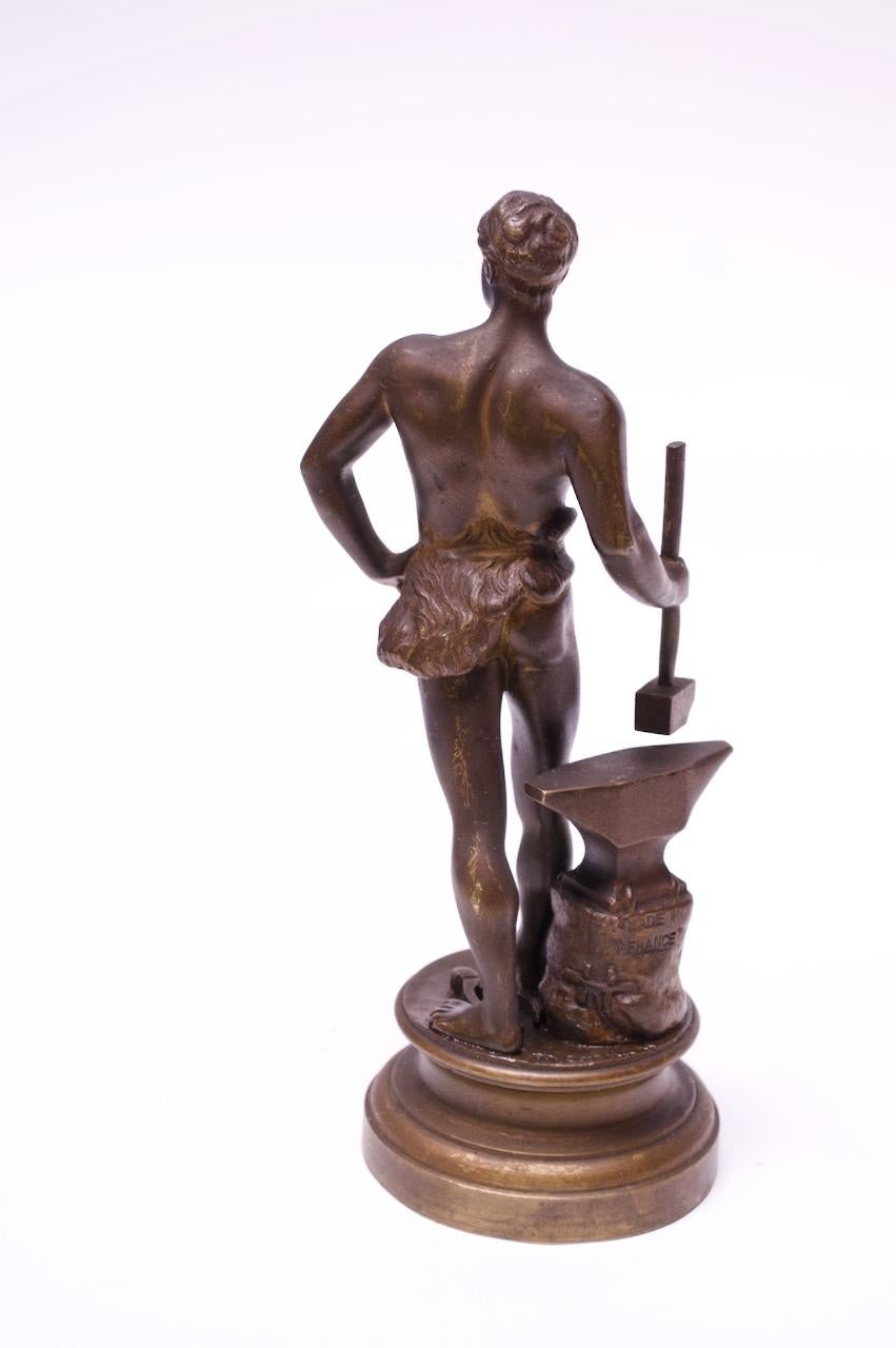 Circa 1920s bronze sculpture by Maurice Constant (France 1892-1970). Likely, a depiction of a young Hephaestus / Vulcan, the blacksmith god of fire and forge, surrounded by his signature tools: hammer, anvil, and tongs.
Signed 