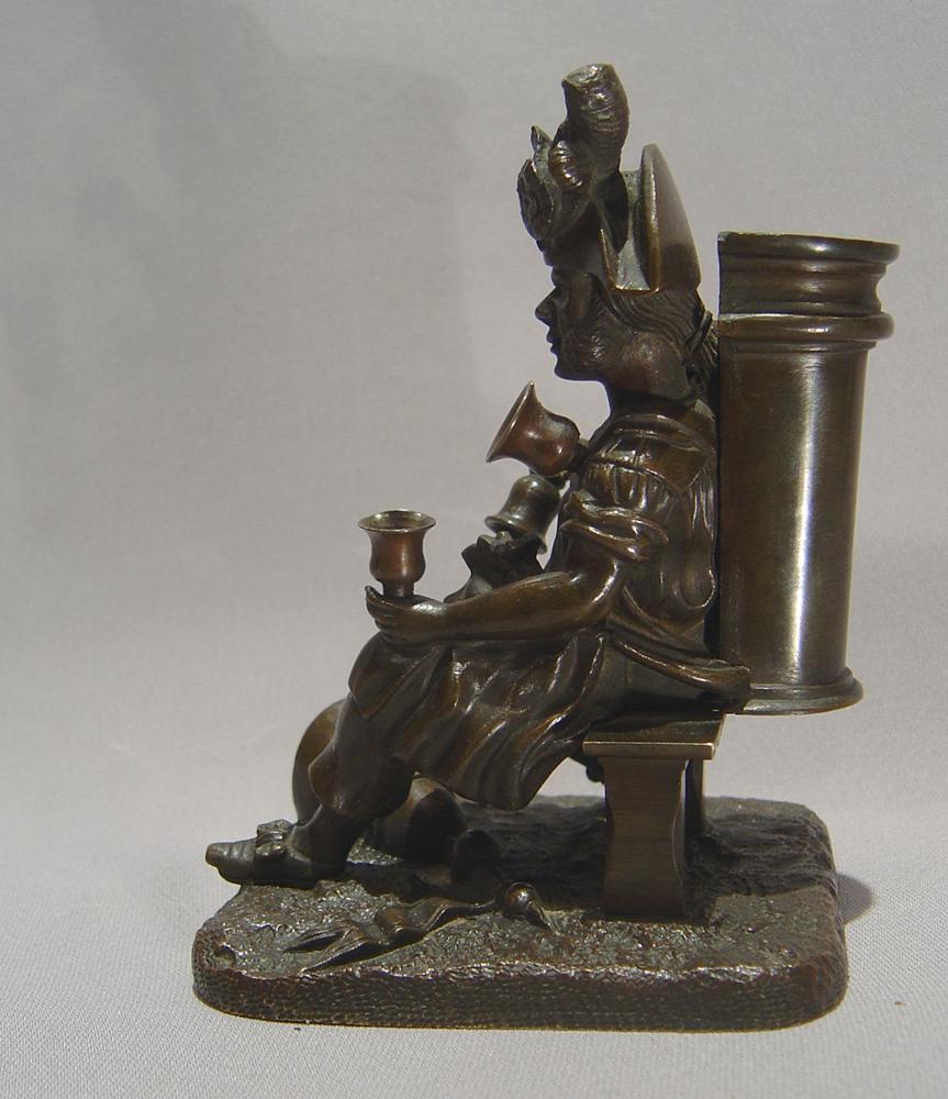 A very well cast and interesting French patinated bronze match strike. It is in the form of a water seller, in the uniform of an old Republican soldier, sitting on a bench. He is seen wearing a tricorn hat with a cockade to the brim, mutton chop