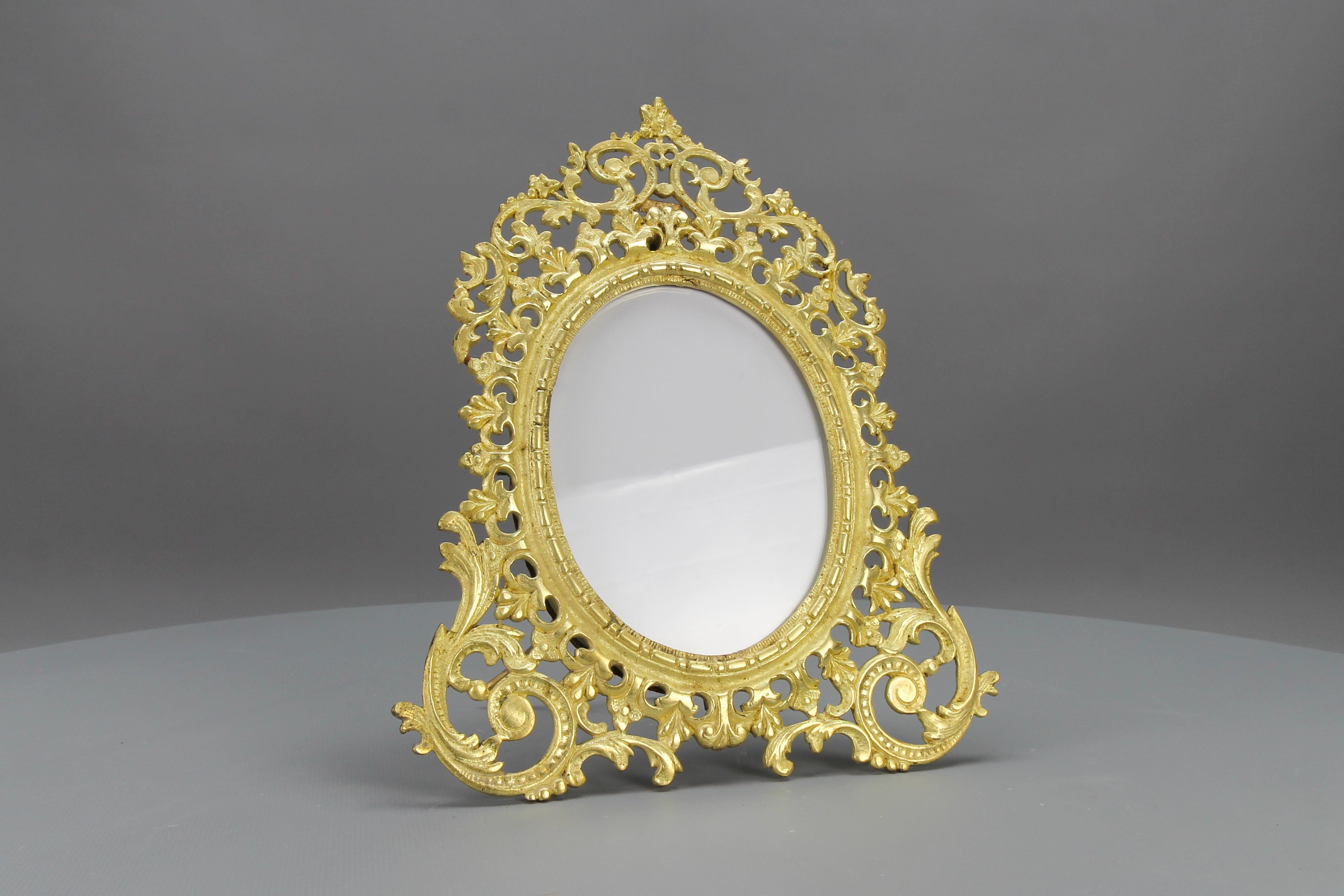 French Bronze Neoclassical Style Round Desktop Picture Frame from circa the 1890s.
This beautiful ornate oval frame is made of bronze and has a supporting leg on the back. Decorated with typical Neoclassical or Louis XVI-style foliate motifs around