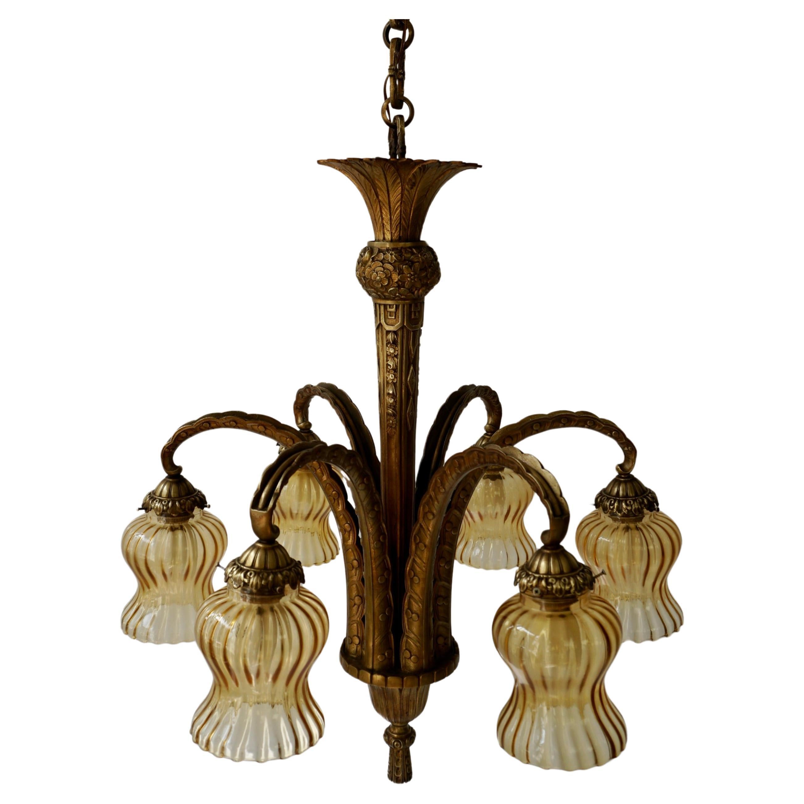 This unique French Art Deco bronze palm chandelier features a captivating and warm gilt bronze finish, with six flowing arms in a beautiful tropical arrangement. Each feather arm is decorated with beautifully shaped amber glasses. Adding to the