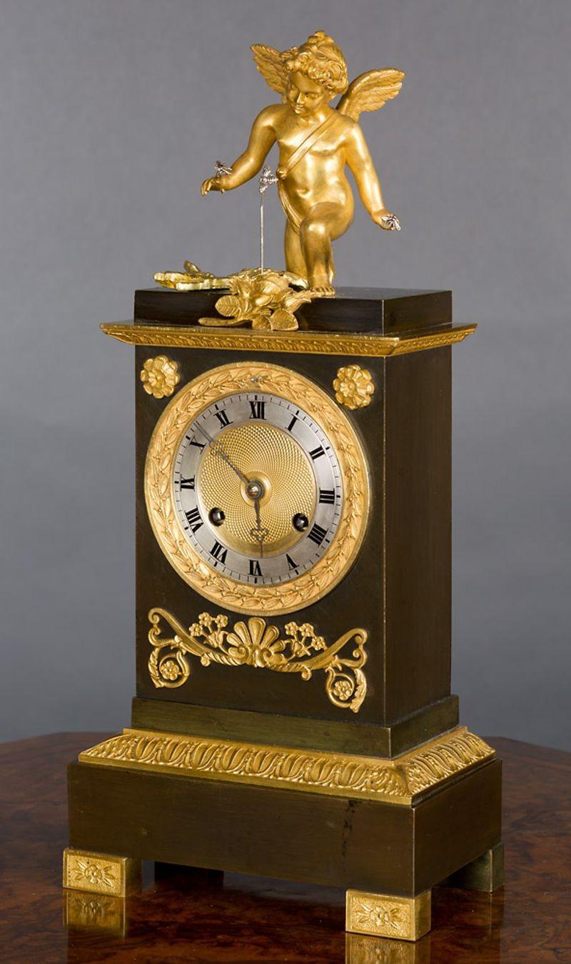 Charles X Bronze and Ormolu mounted mantel clock with stepped top surmounted by a gilded figure of Cupid holding silver Bees and with a rocking silver Bee automation.
The case on a raised plinth with raised gilded decoration and standing on scroll