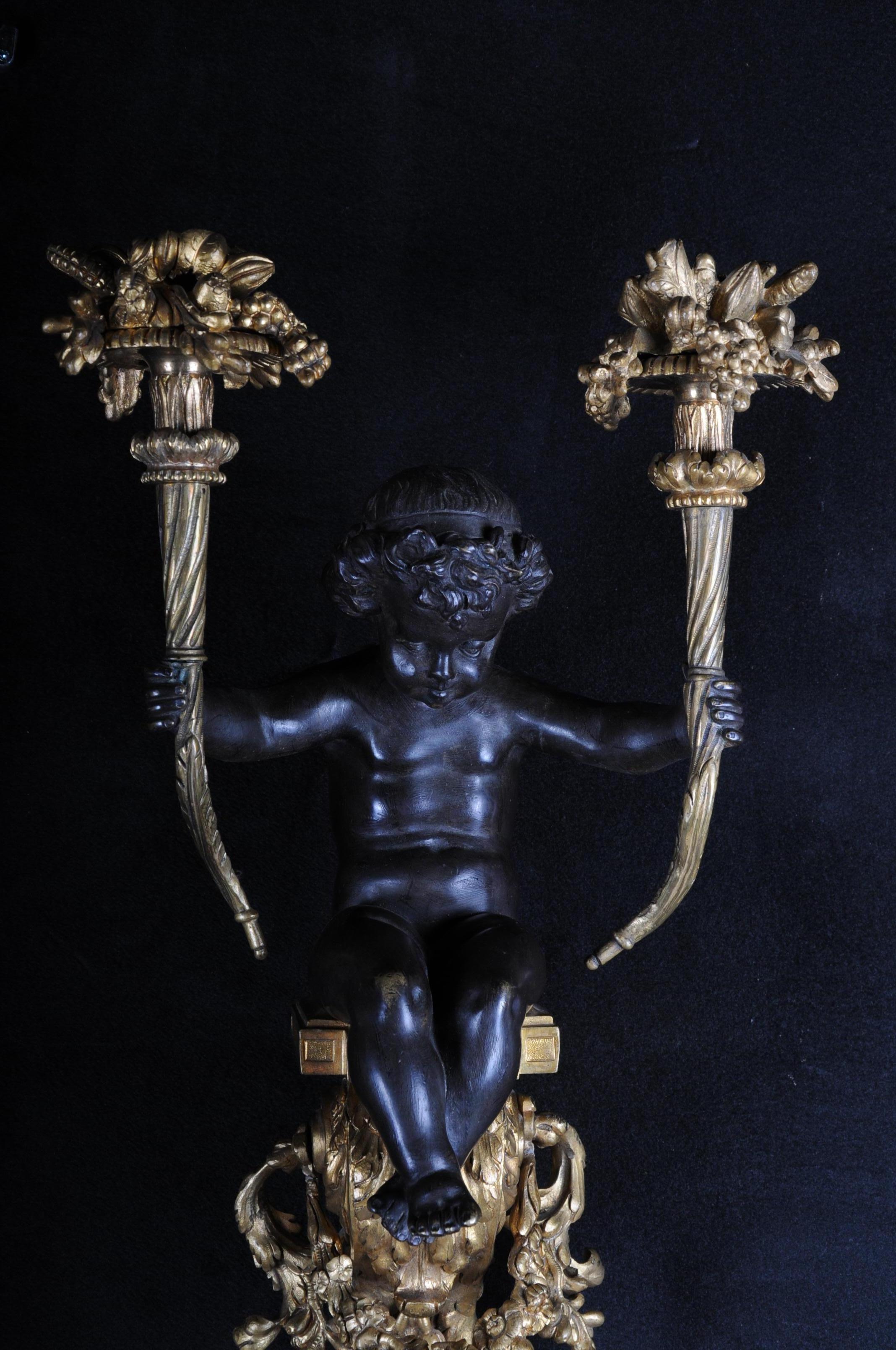 French bronze sconce, appliqué napoleon III, circa 1870.

Unique two-flame appliqué, fire-gilded. In the center sitting a putto holding both lighthouses.
Finely chiseled and gilded.
Appliqué in the style of Louis XVI. Bronze, gilded, black